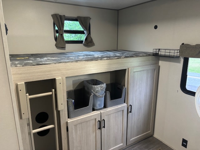 Cozy RV rental bunk area features a comfortable bed, convenient storage cabinets, bins, and a ladder for easy access, ideal for family trips.. Forest River Aurora Aurora 2024