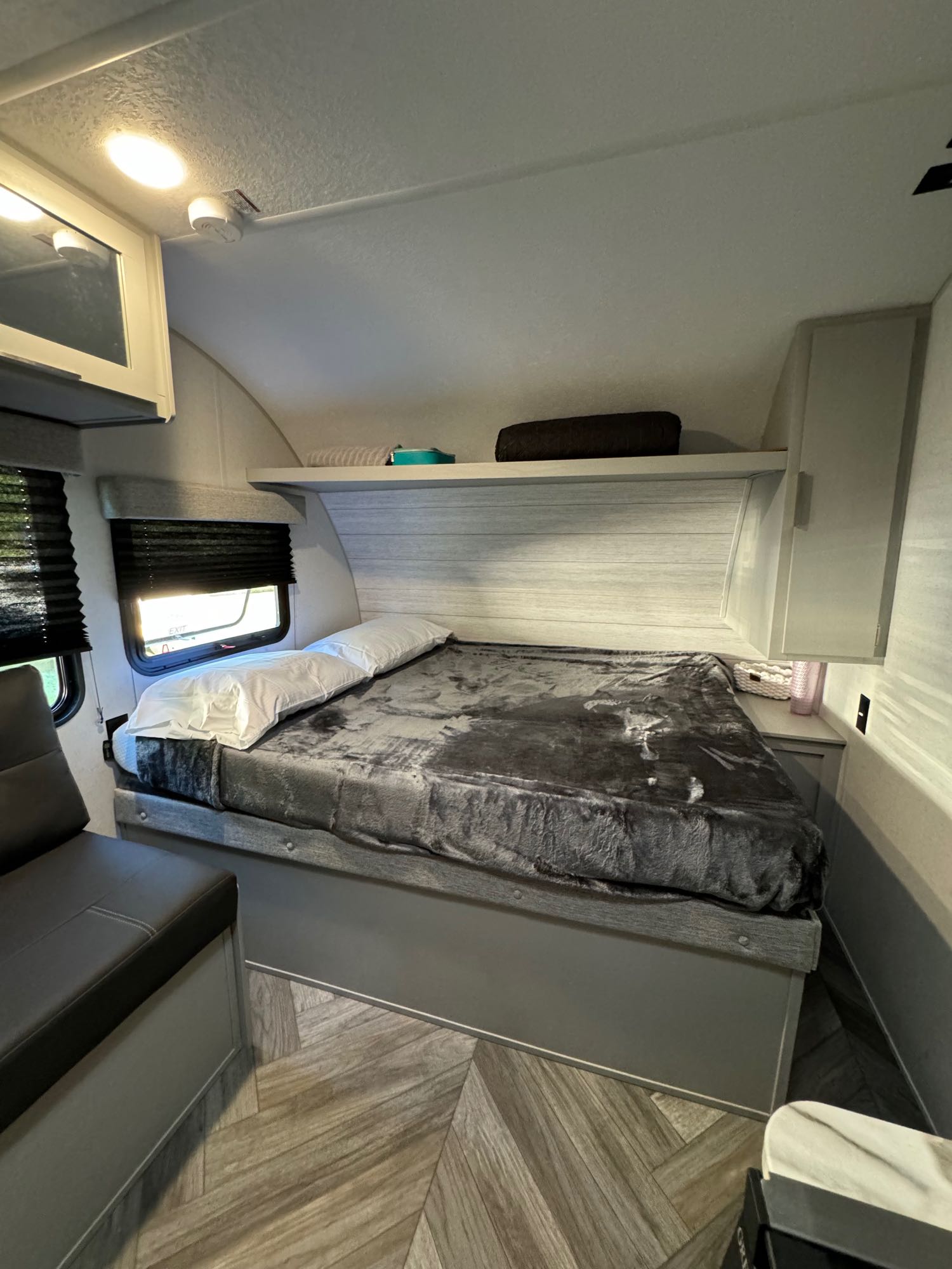 Cozy RV rental bedroom featuring a large bed, seating, modern grey decor, and chevron flooring. Ideal for travel.. Forest River Wildwood FSX 2023