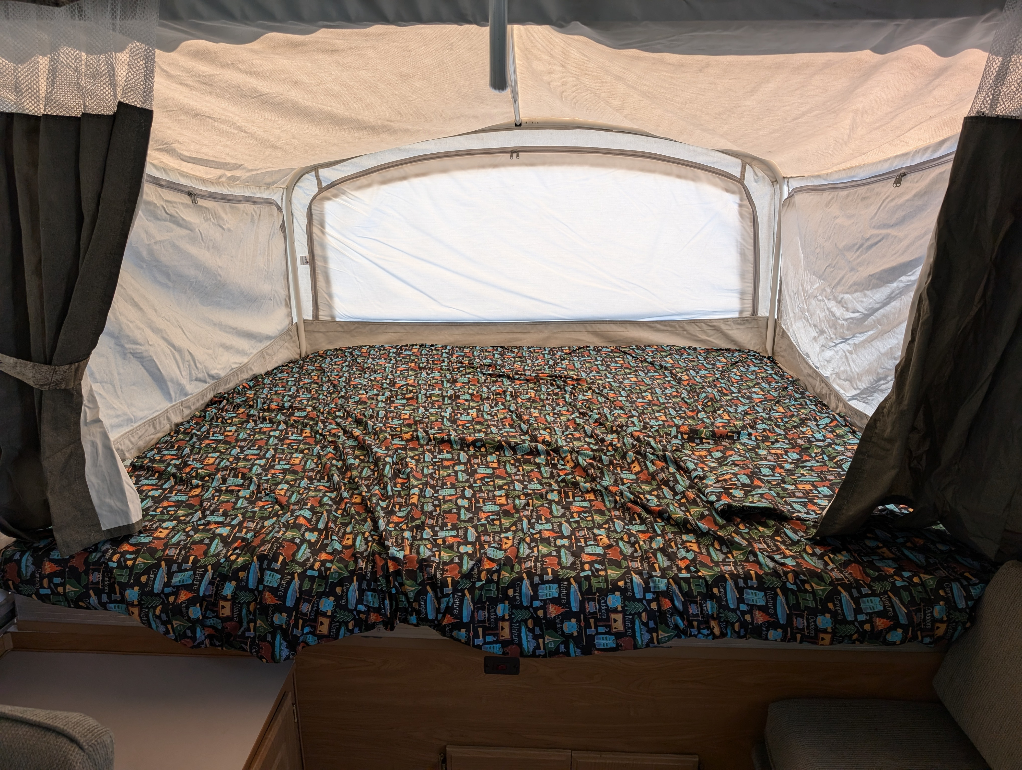 Cozy pop-up camper bed in an RV rental, featuring vibrant camping-themed bedding and interior tent walls with curtains.. Coleman Utah 2003