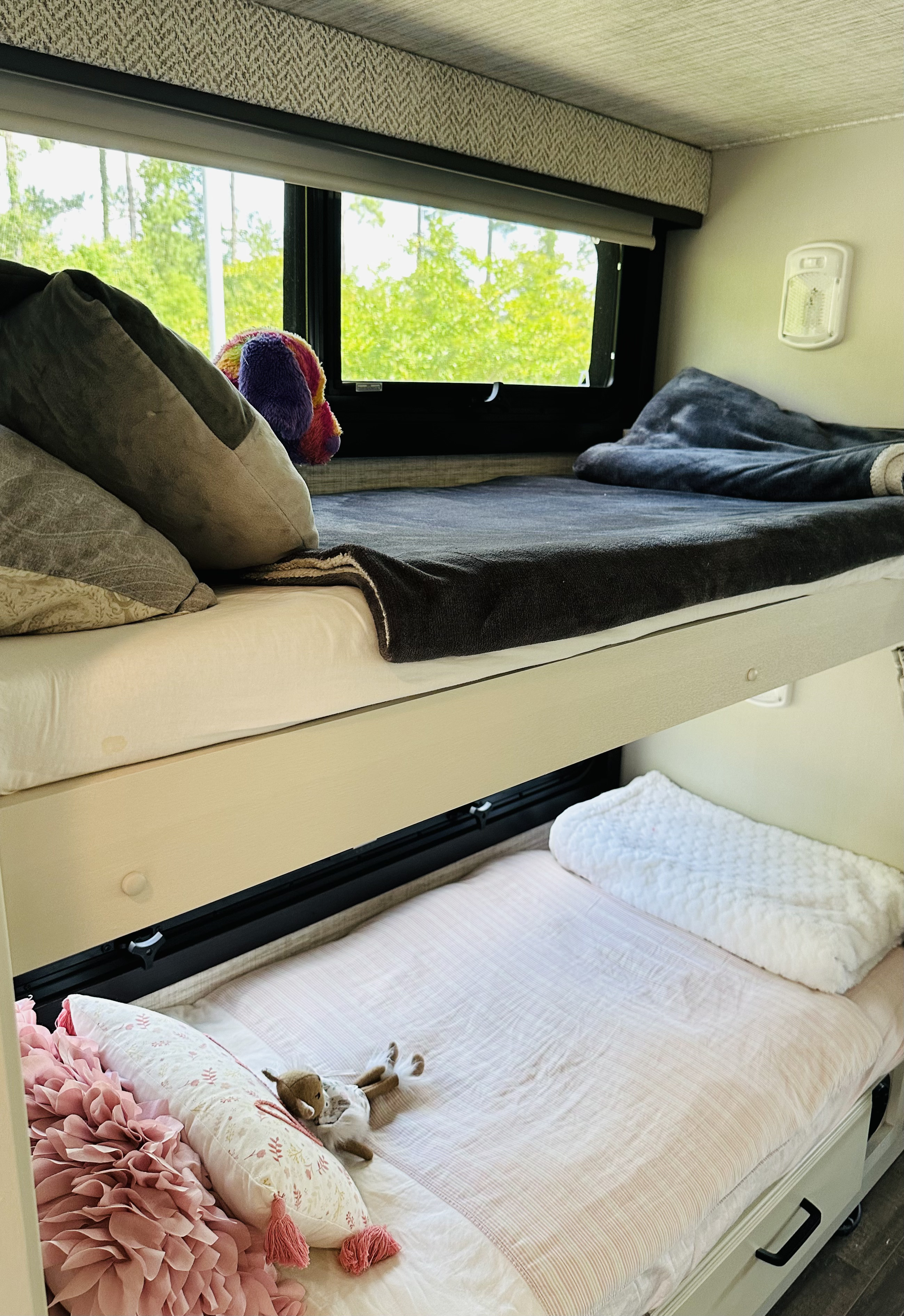 Cozy RV rental bunk beds: two comfortable sleeping areas with pillows, blankets, and a window showing green trees outside.. Jayco Alante 29F 2024