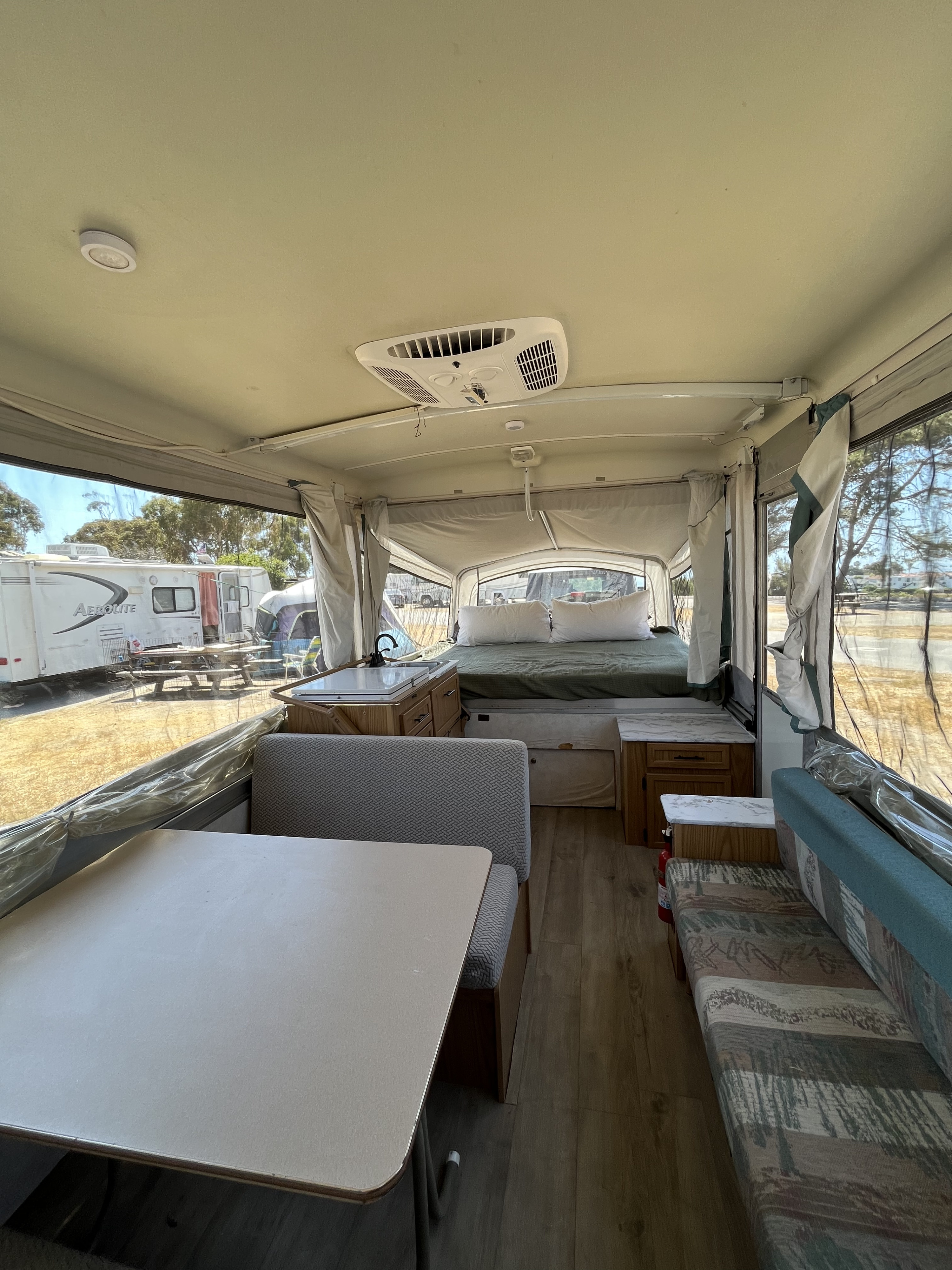 Inside a pop-up RV rental: a spacious interior with a bed, dinette, small kitchen, and an air conditioning unit visible.. Coleman Destiny Cheyenne 1998