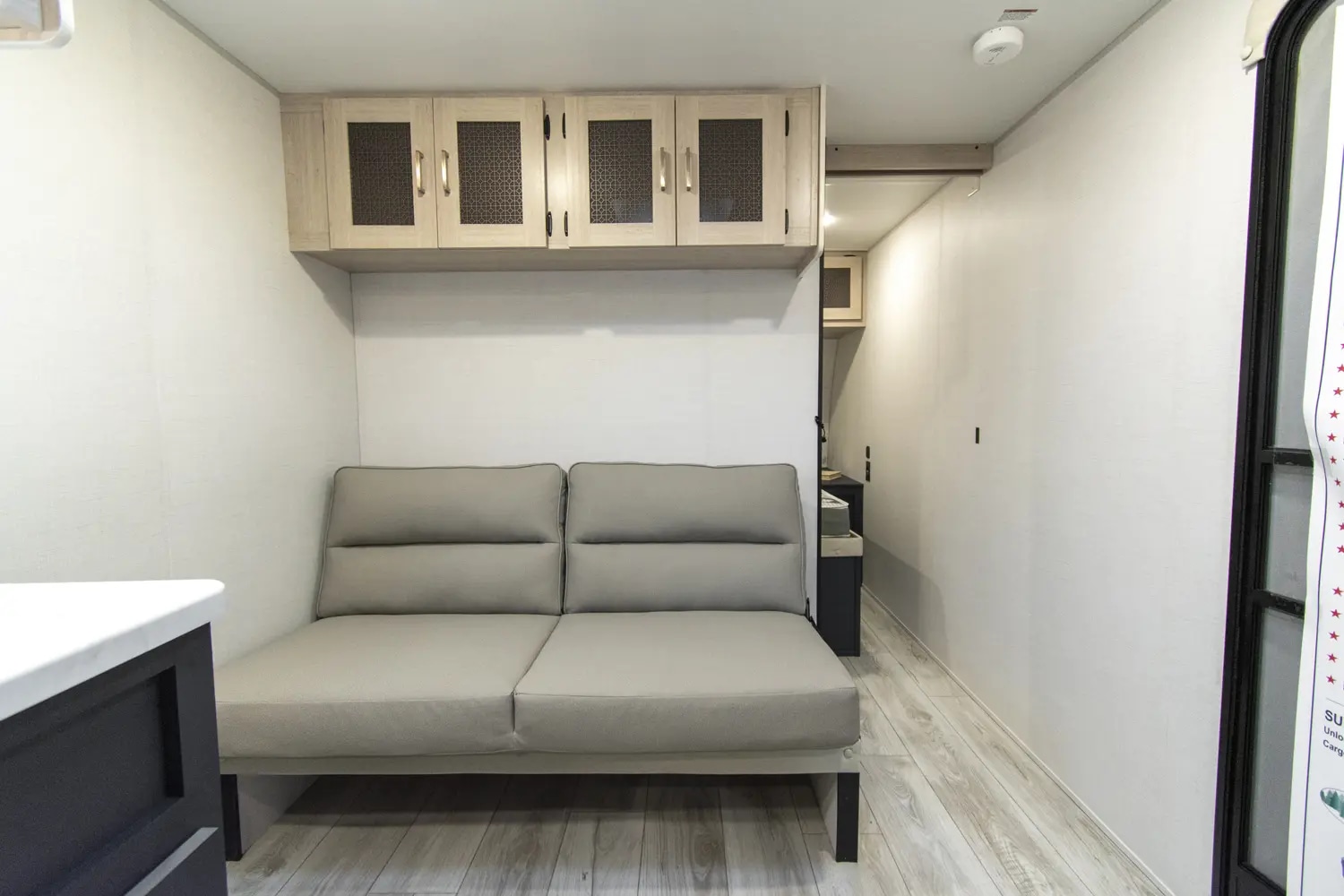Spacious RV rental interior featuring a light grey sofa, overhead storage cabinets, and clean white walls, perfect for comfortable travel.. Primetime RV 25 BH 2024