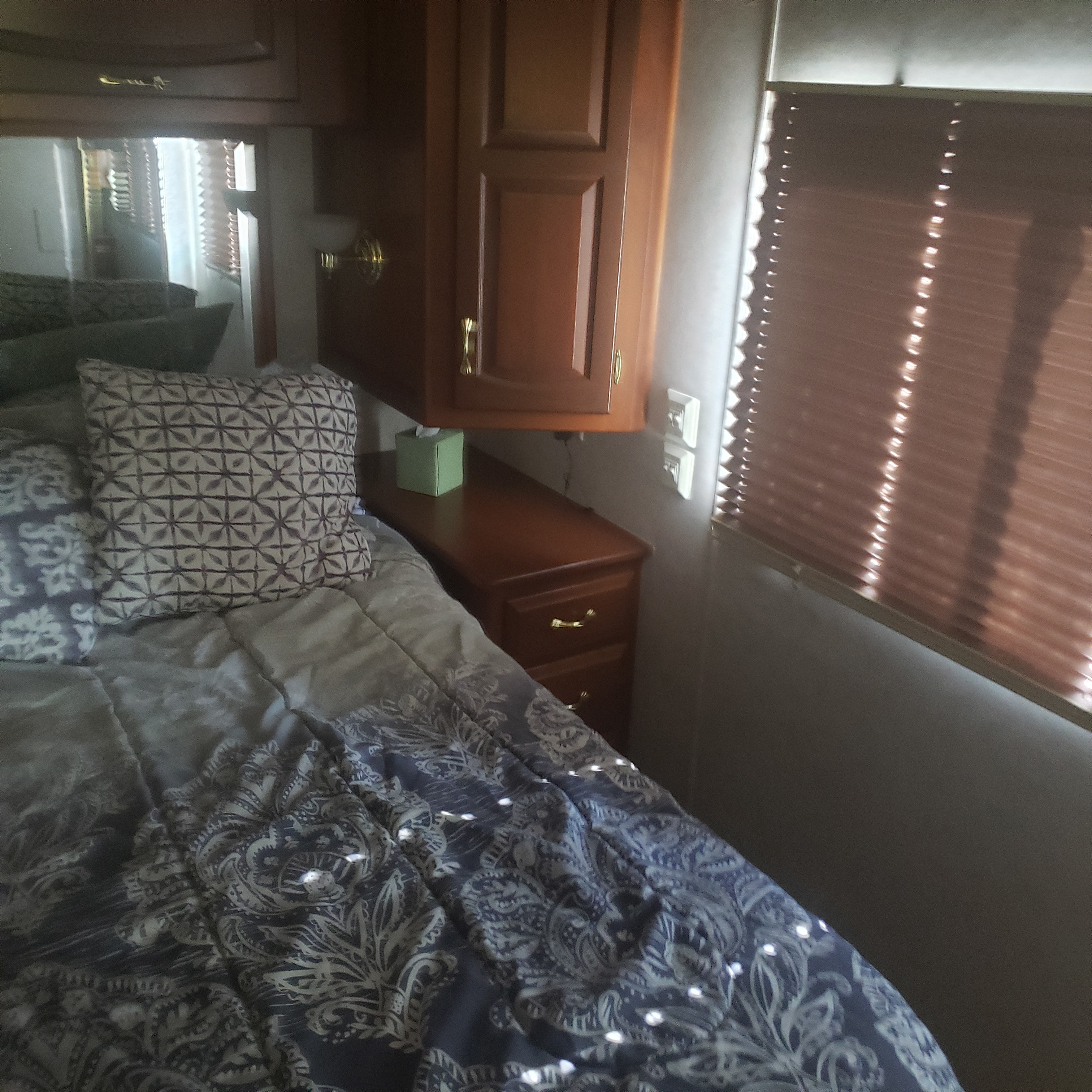Cozy RV rental bedroom featuring a bed with patterned bedding, wooden cabinets, and blinds, perfect for your next adventure.. Newmar Mountain Aire 1998