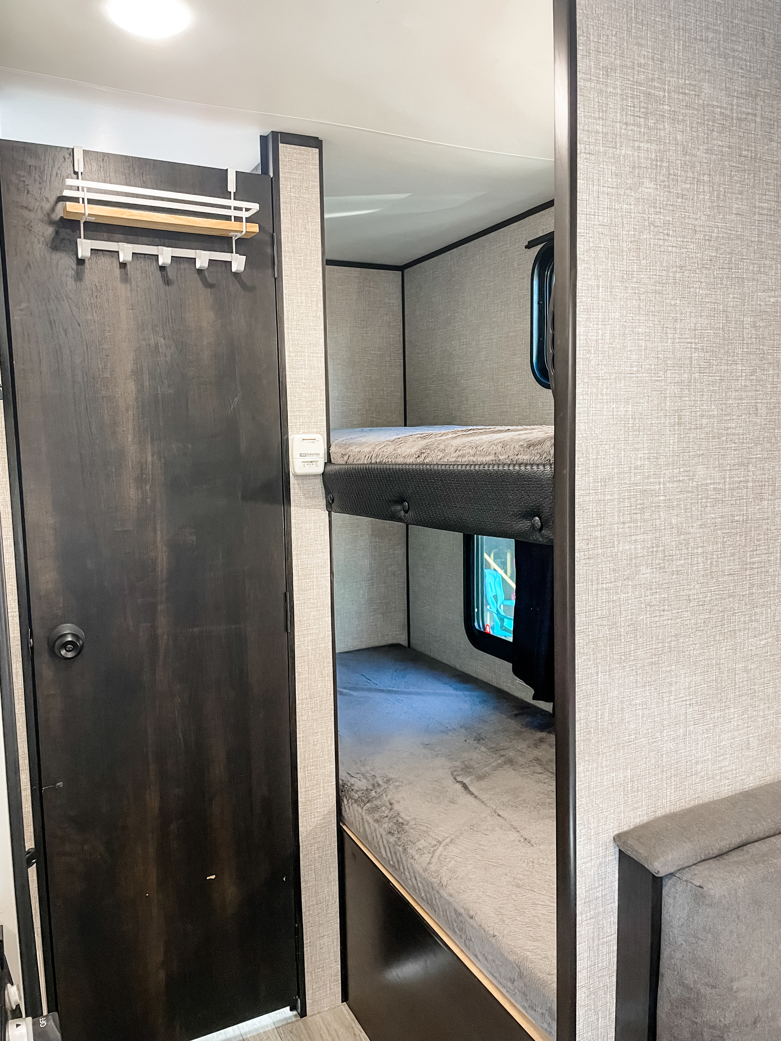 This RV rental interior features comfortable bunk beds, a dark wood door with a convenient organizer, and a wall-mounted thermostat.. Jayco Jay Flight SLX Baja Edition 2022