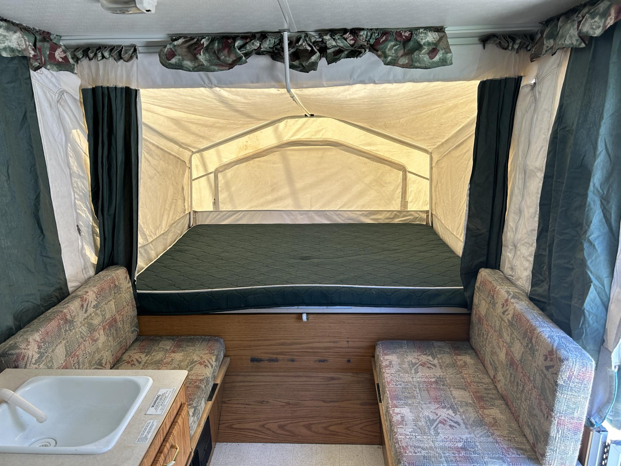 Spacious pop-up camper interior for your next RV rental adventure, featuring a large bed, dinette, and sink.. Rockwood Freedom 1998