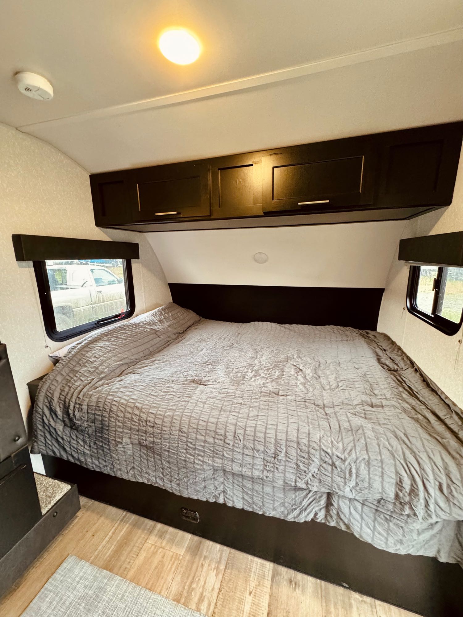 Inside this RV rental bedroom, a cozy bed with gray bedding, dark overhead cabinets, and windows offer comfort.. Forest River Cherokee Wolf Pup 2022