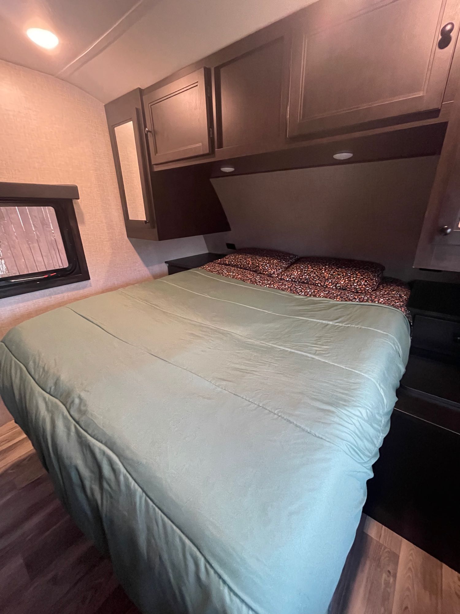 Cozy RV rental bedroom with dark wood cabinetry, a light green comforter, and patterned pillows.. Highland Ridge RV Mesa Ridge S-Lite 2023