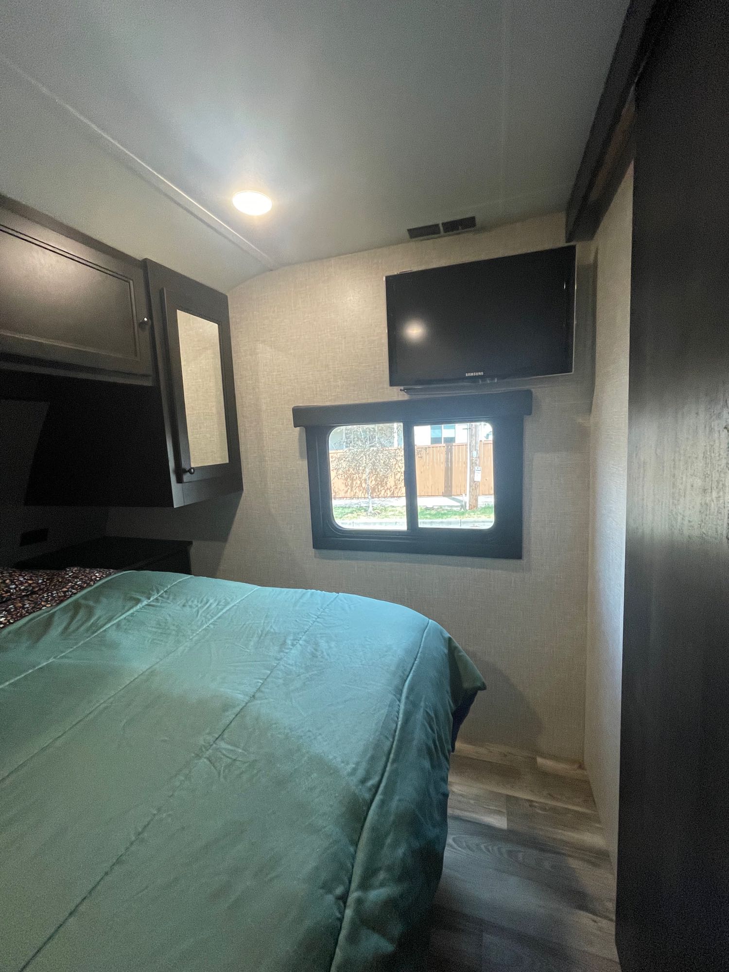 RV rental bedroom: green bed, wall-mounted TV, window view, dark overhead cabinets. A compact, comfy travel space.. Highland Ridge RV Mesa Ridge S-Lite 2023