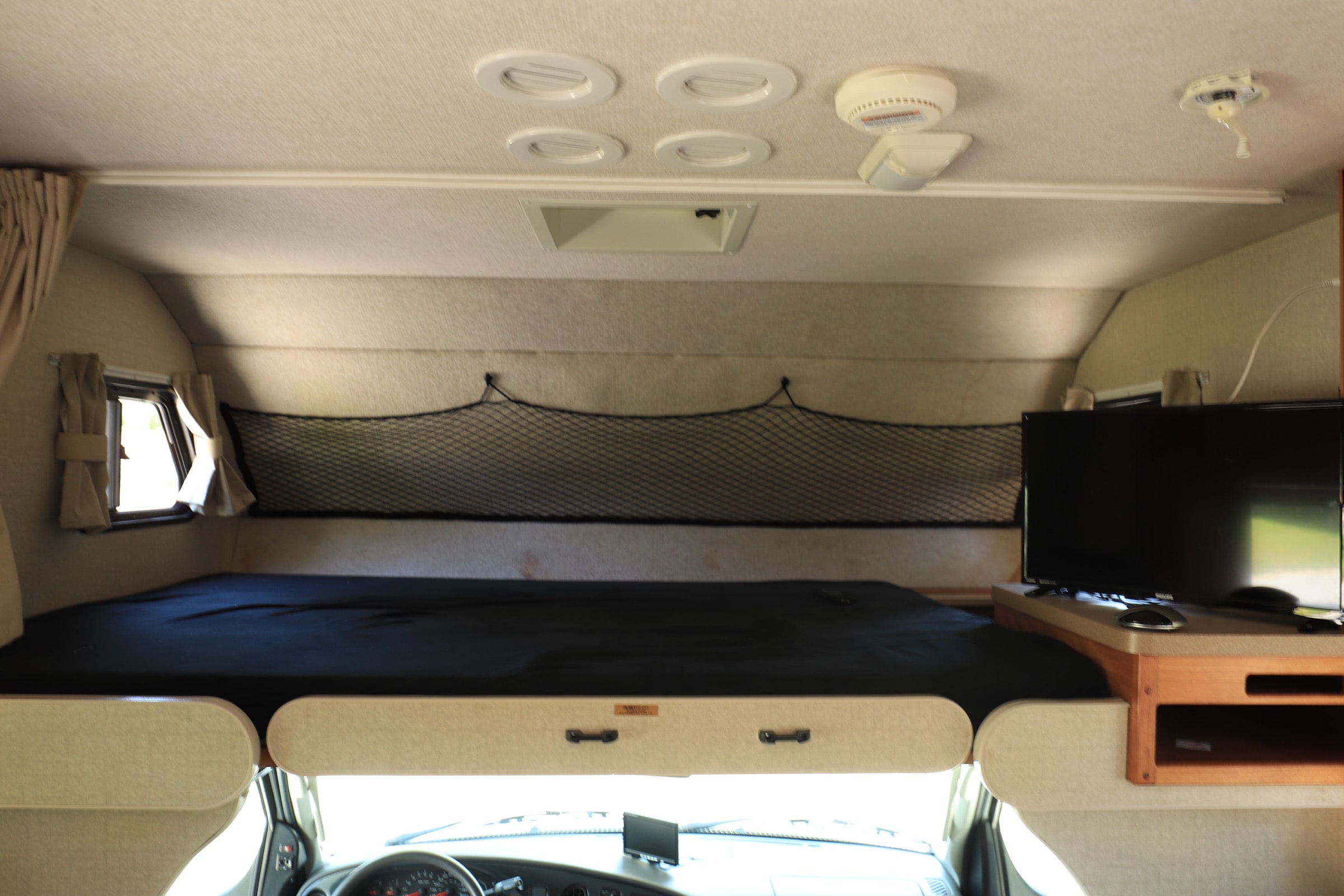 Inside an RV rental: cozy cab-over bunk bed with safety net, window, and TV.. Fleetwood Tioga 31m 2007