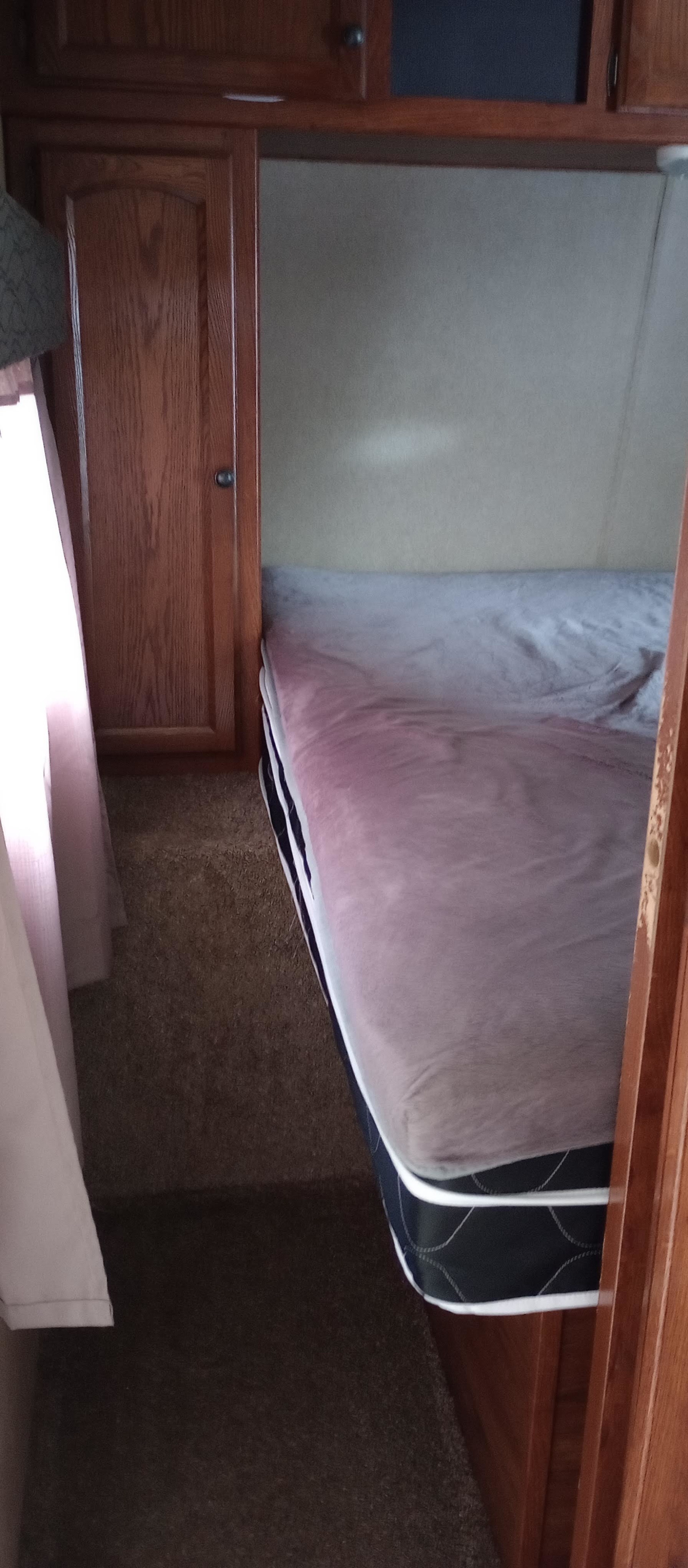 Inside an RV rental: a cozy bedroom with a bed, wood cabinetry, and carpeted floor. Compact sleeping area.. Keystone Hideout 2015