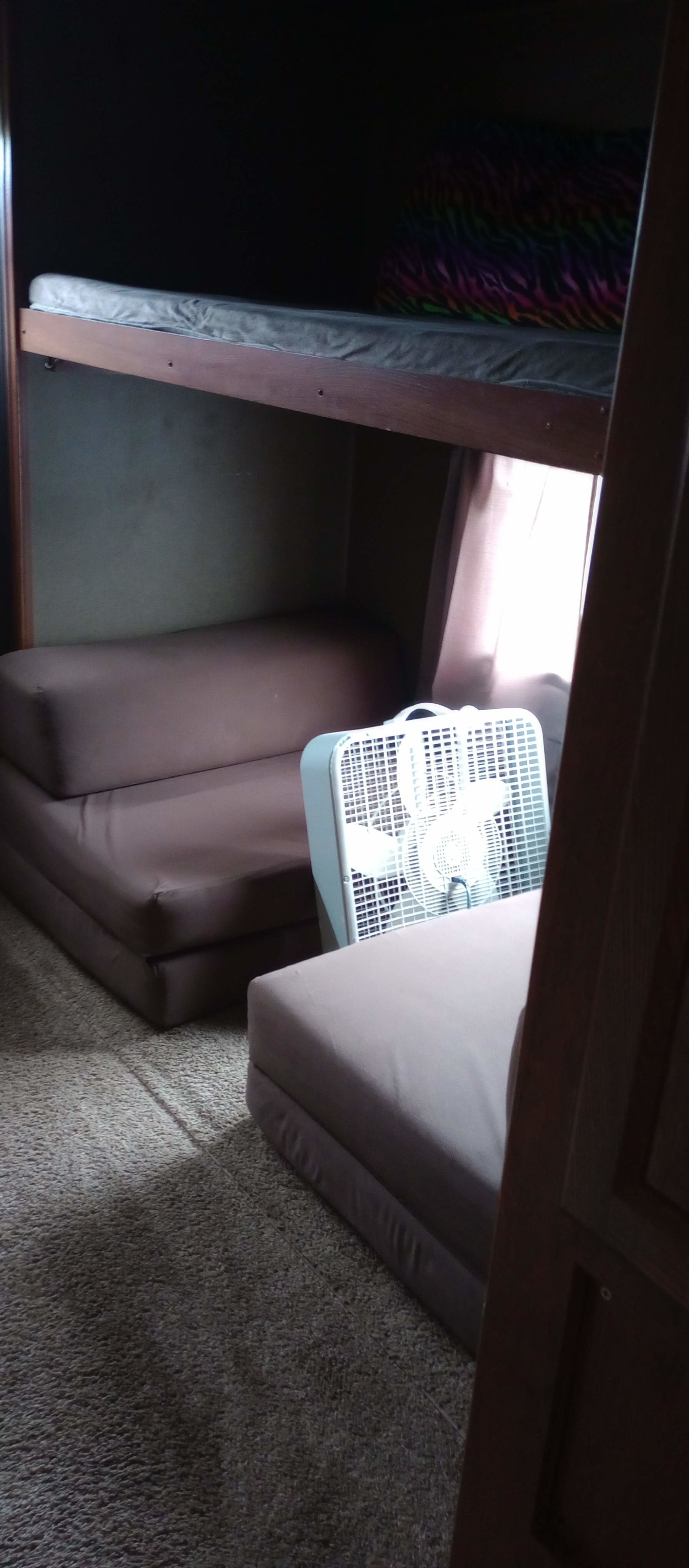 Inside an RV rental: bunk beds above a foldable sofa and a fan on the carpeted floor, offering a functional sleeping area.. Keystone Hideout 2015