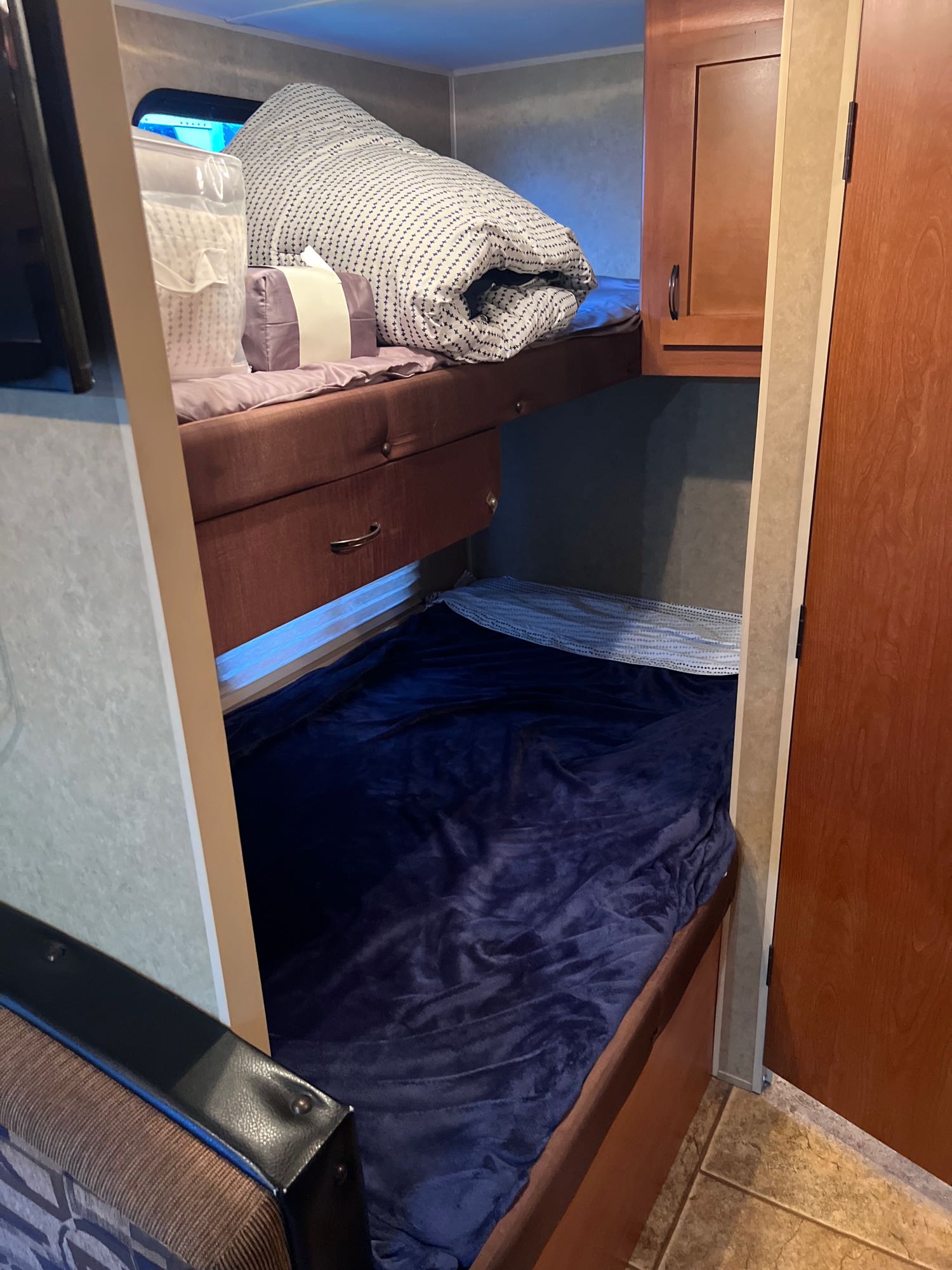 RV rental bunk beds: The upper bed has folded patterned bedding, a packaged pillow & purple pillow. Lower bed with dark blue blanket.. Forest River Cherokee Grey Wolf 2013