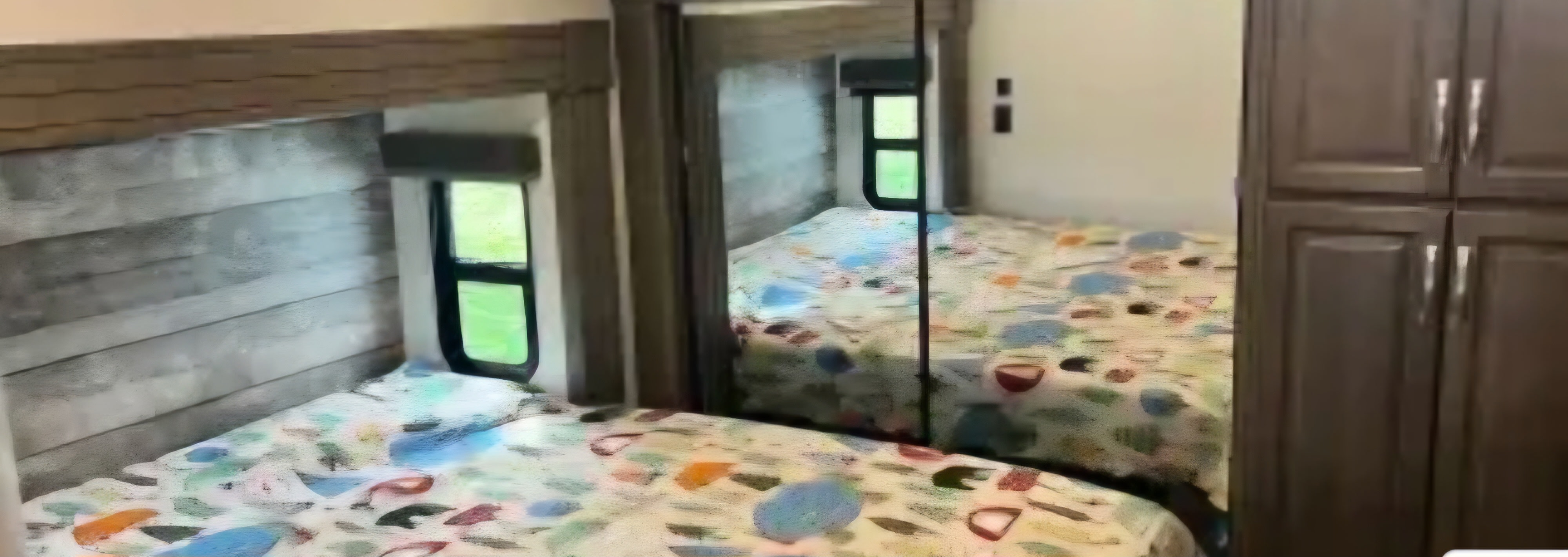 Comfortable RV rental bedroom with colorful patterned bedding, bright window, and built-in storage.. Keystone RV Cougar 2021