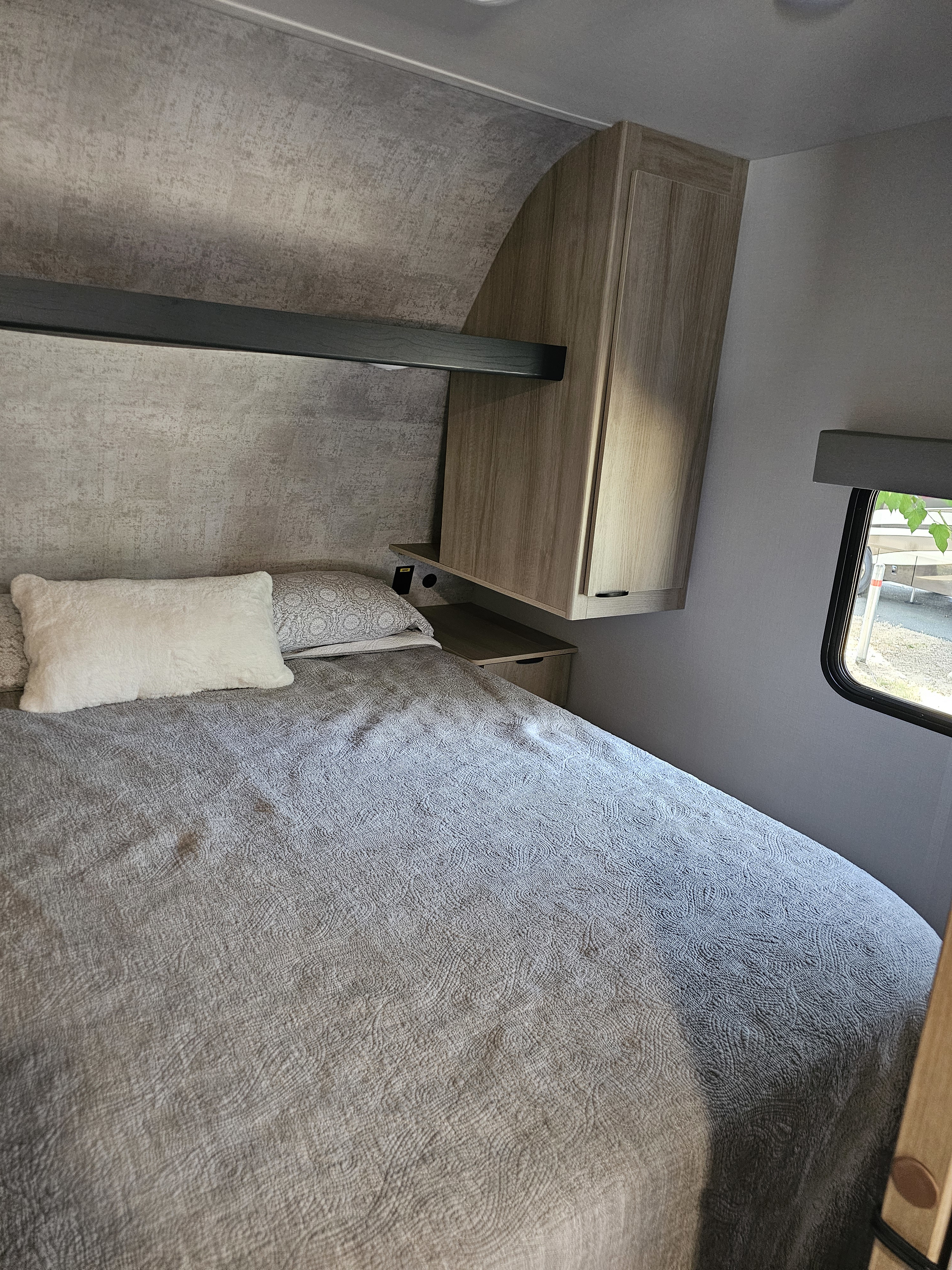 Cozy RV rental bedroom with gray bed, overhead storage, and window view. Perfect for your next adventure.. Winnebago Minnie 2301BHS 2024