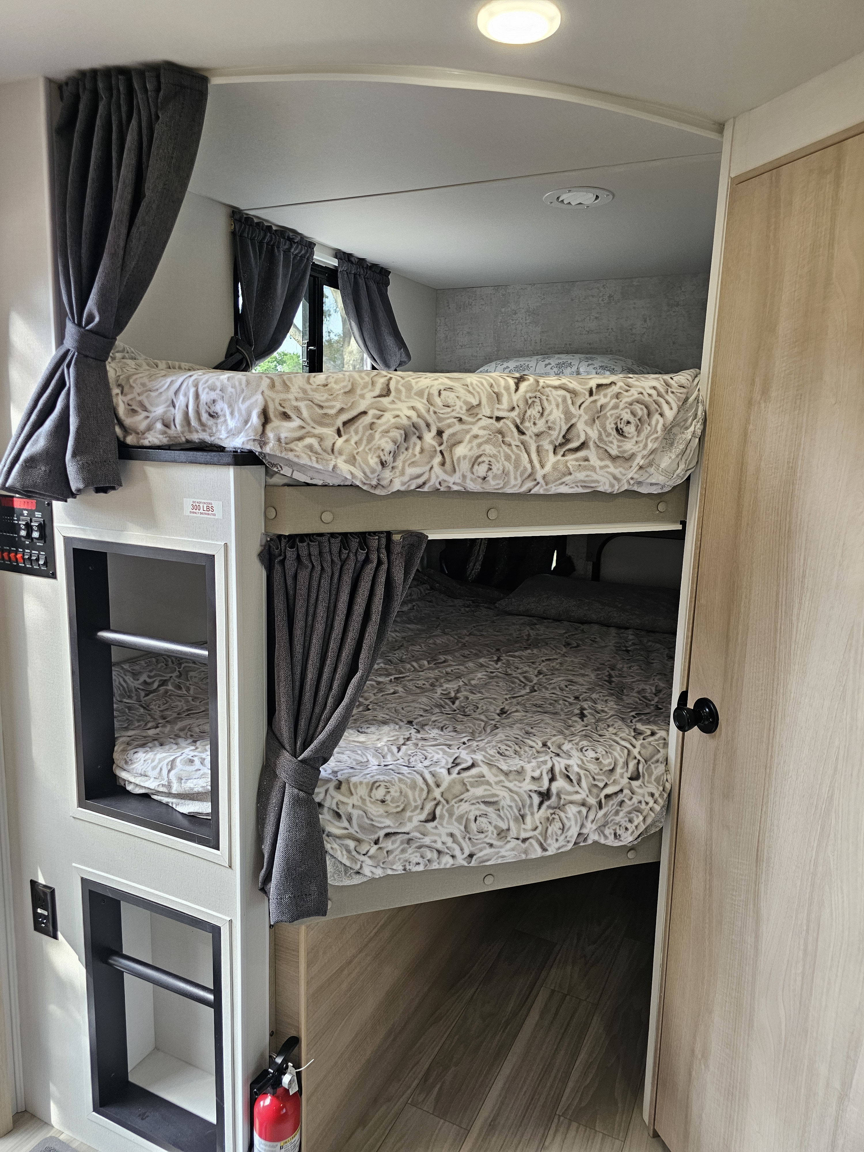 Modern rv rental interior features comfortable bunk beds with curtains, built-in storage, and a fire extinguisher.. Winnebago Minnie 2301BHS 2024
