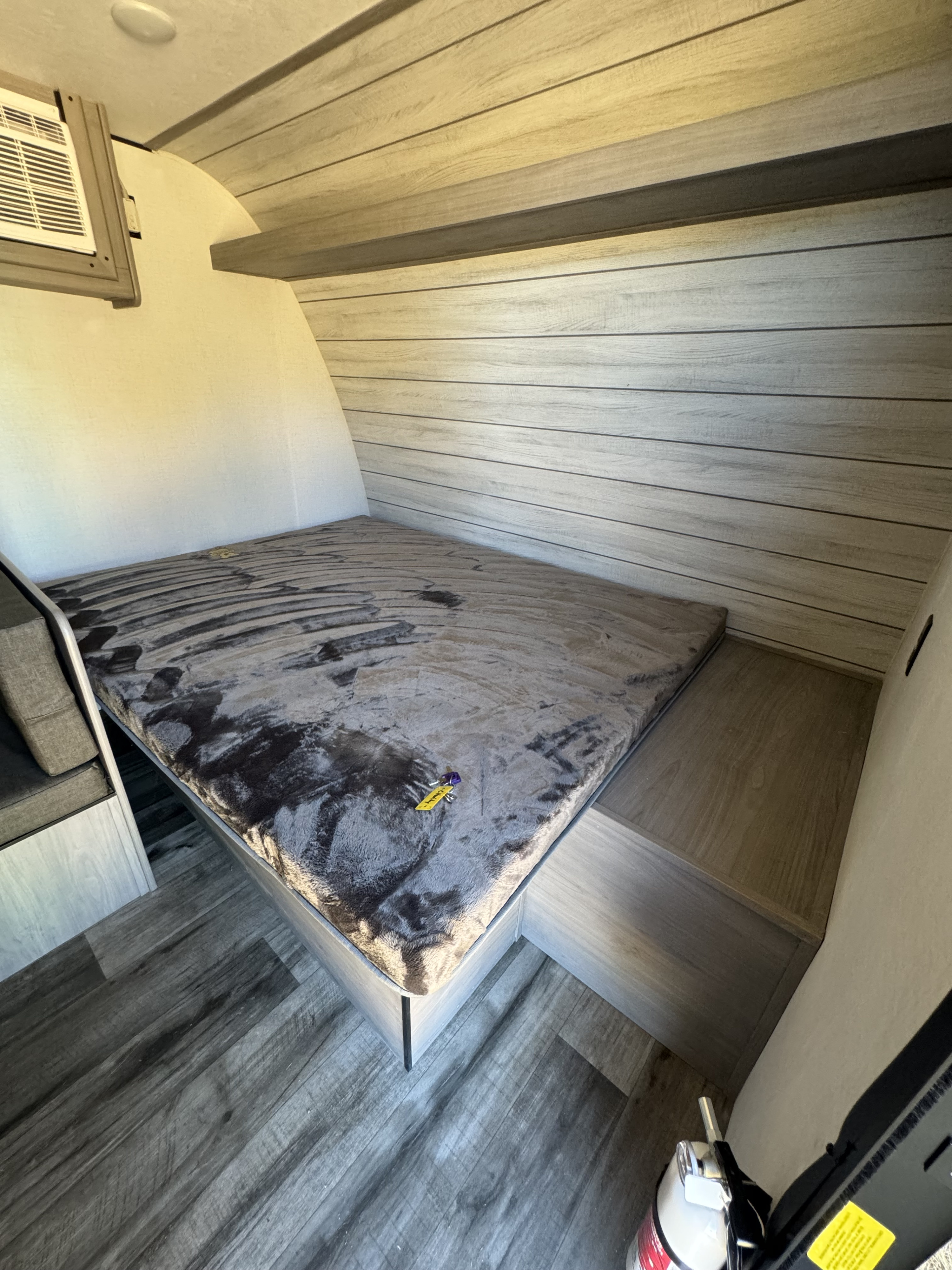 Explore this cozy rv rental interior, featuring a compact bed, wood-paneled walls, an A/C unit, and built-in storage.. Dutchmen Coleman Lantern 2024