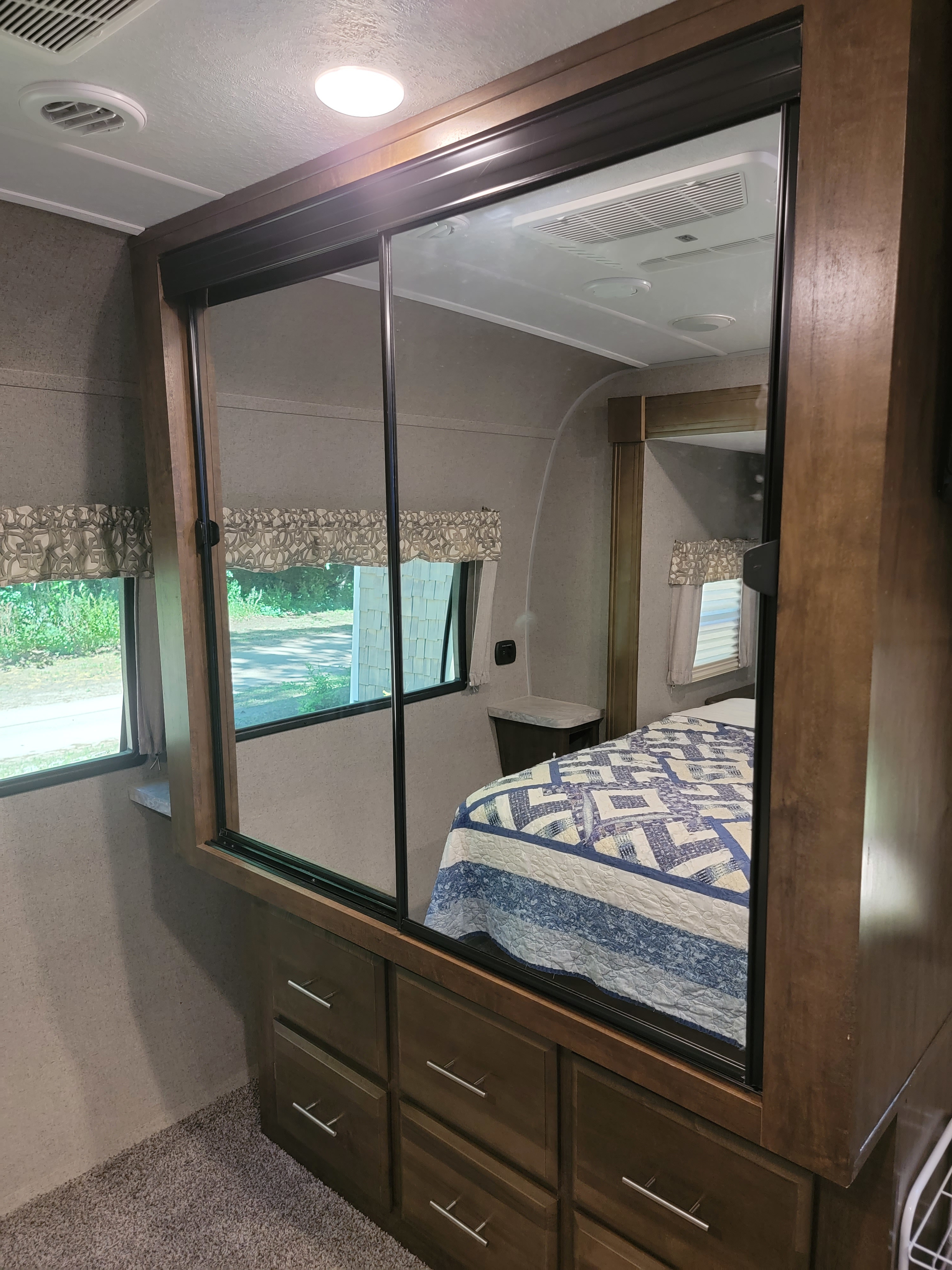 Inside this RV rental, a bedroom features a quilt-covered bed reflected in a sliding mirrored closet, with ample drawer storage.. Forest River Rockwood Signature 2020