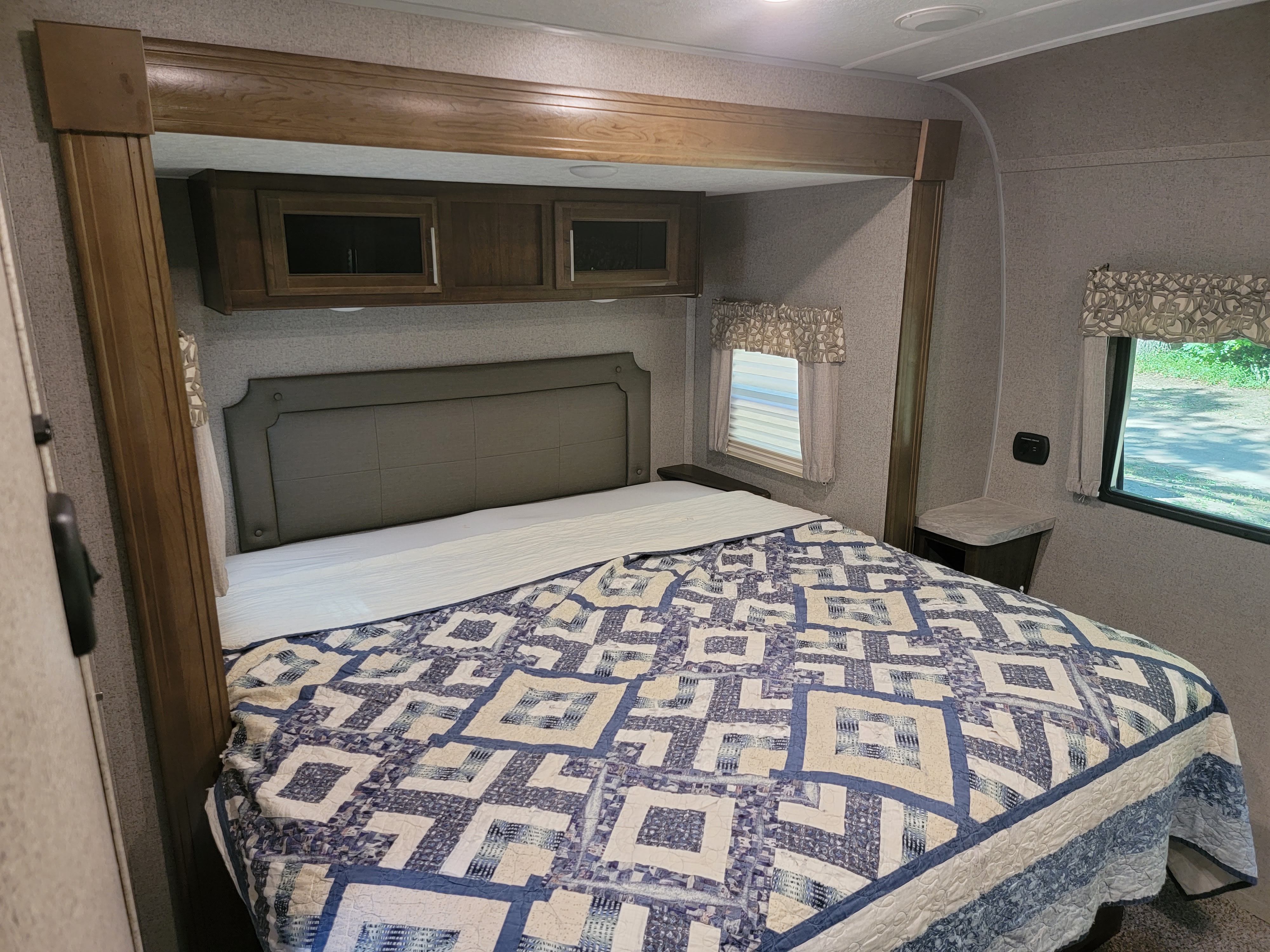 RV rental bedroom: Comfy bed with blue quilt, padded headboard, wooden cabinets, and window.. Forest River Rockwood Signature 2020