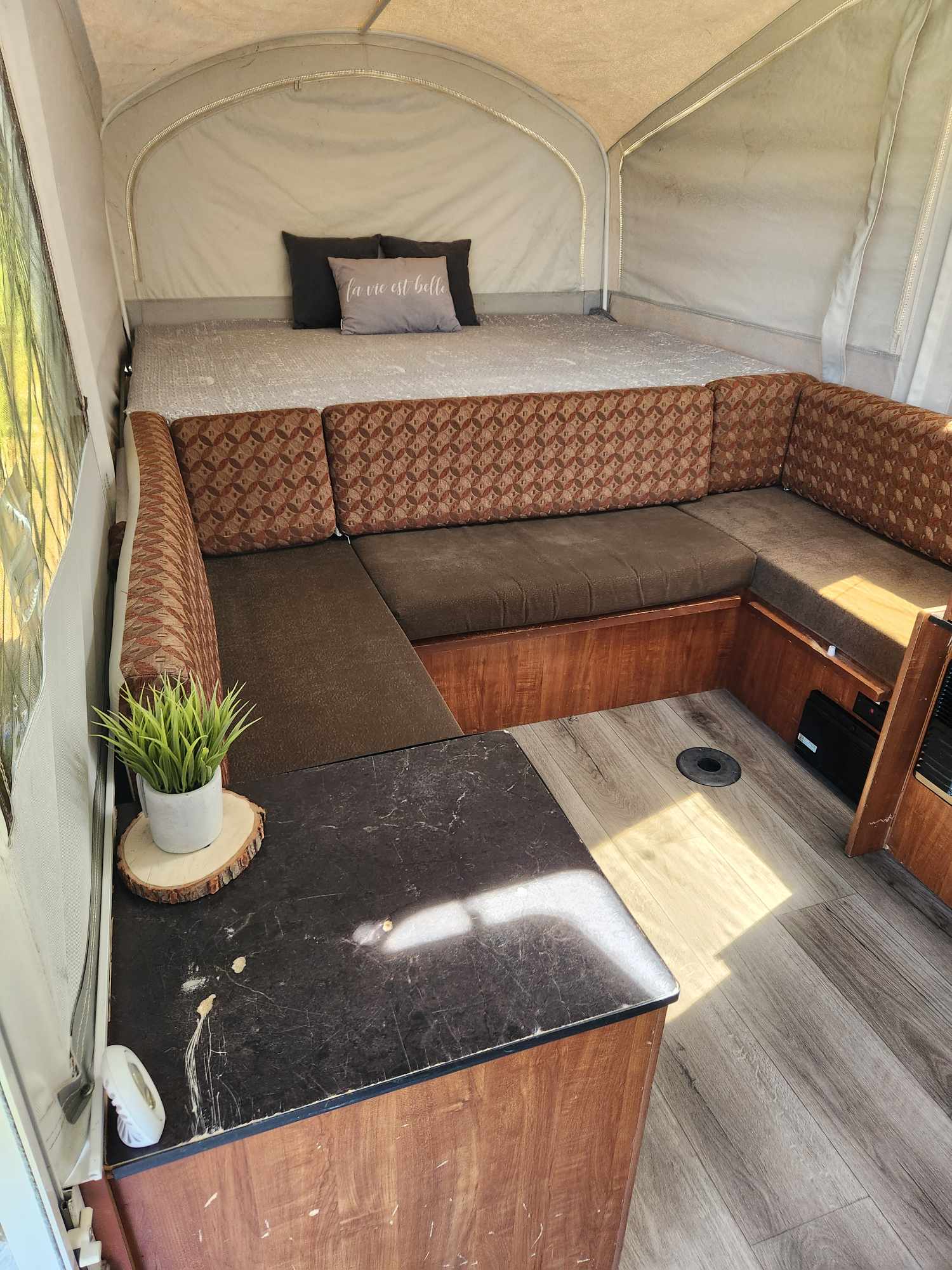 Pop-up camper interior showing a bed, U-shaped dinette with patterned cushions, and wood-look floor. Great RV rental!. Jayco Jay 2014