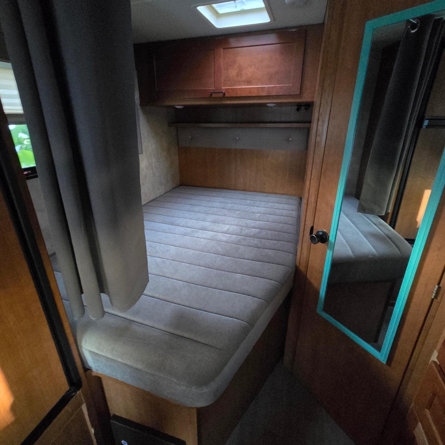 This RV rental's cozy bedroom features a comfortable gray mattress, wood cabinets, a privacy curtain, and a door mirror.. Winnebago Minnie Winnie 2019