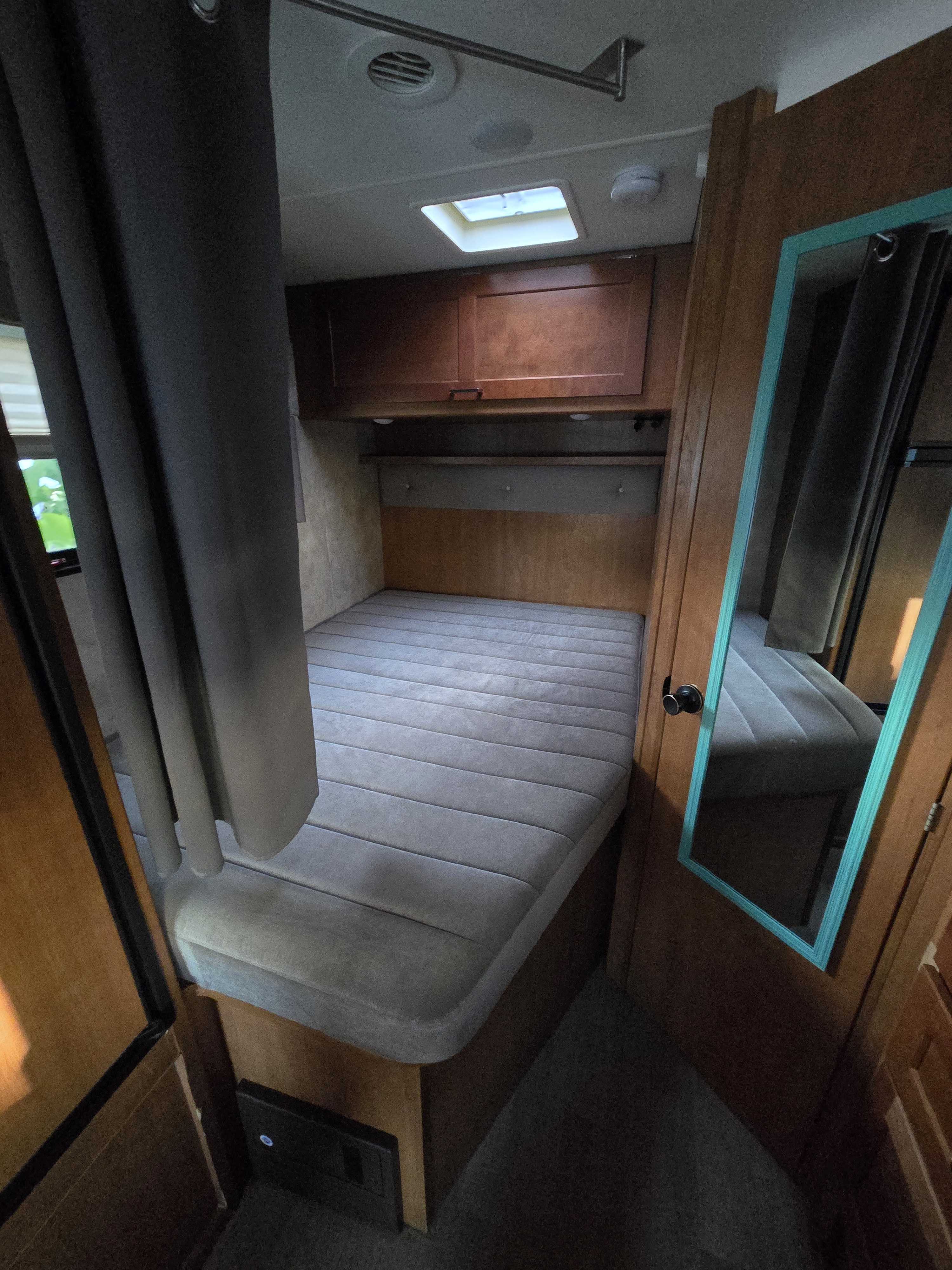Inside an RV rental: A compact bedroom with a mattress, overhead storage, skylight, and wall mirror near the door.. Winnebago Minnie Winnie 2019
