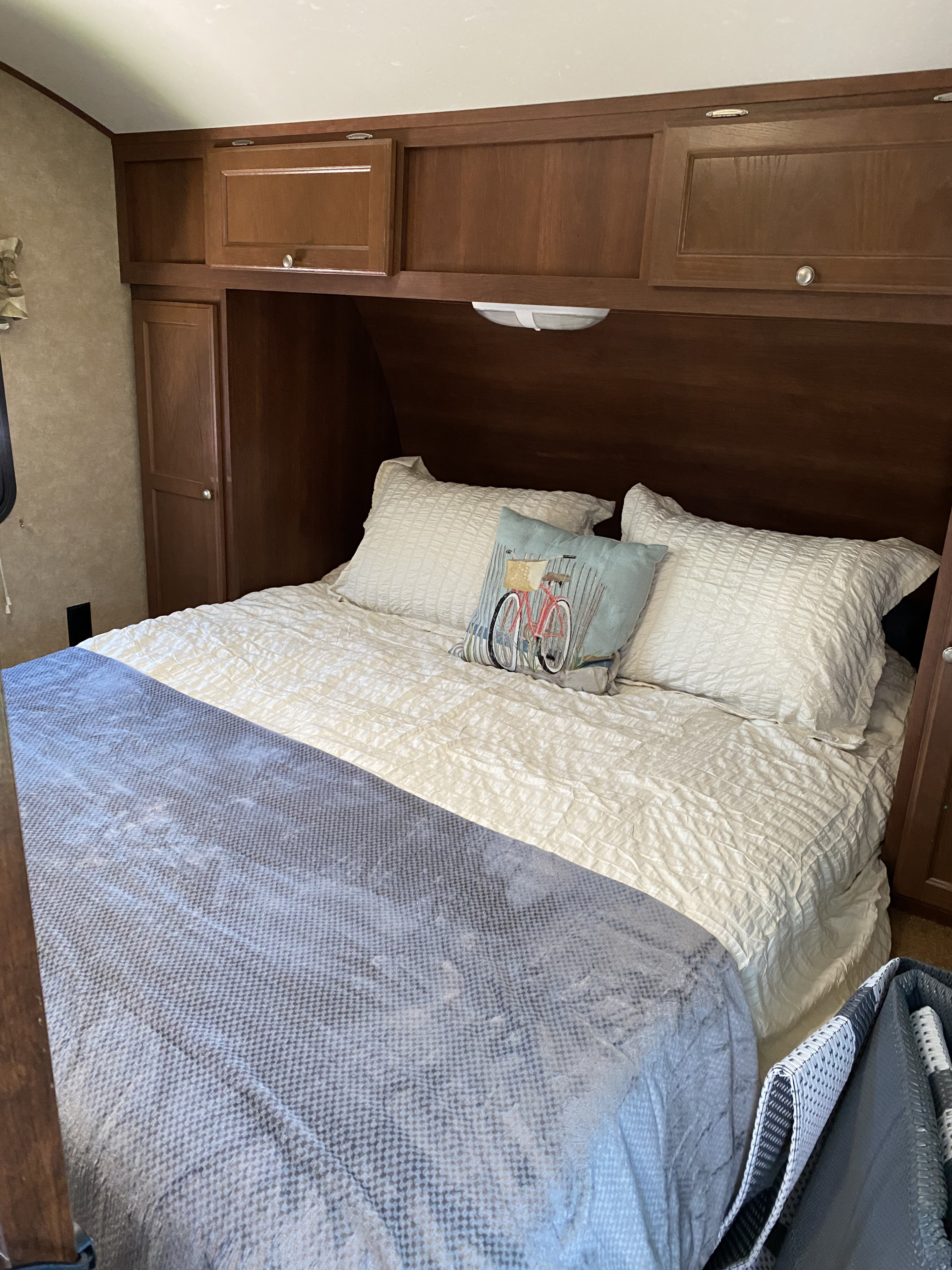 Cozy RV rental bedroom with a comfortable bed, white bedding, blue throw, and wooden overhead storage.. Crossroads RV Z-1 2013