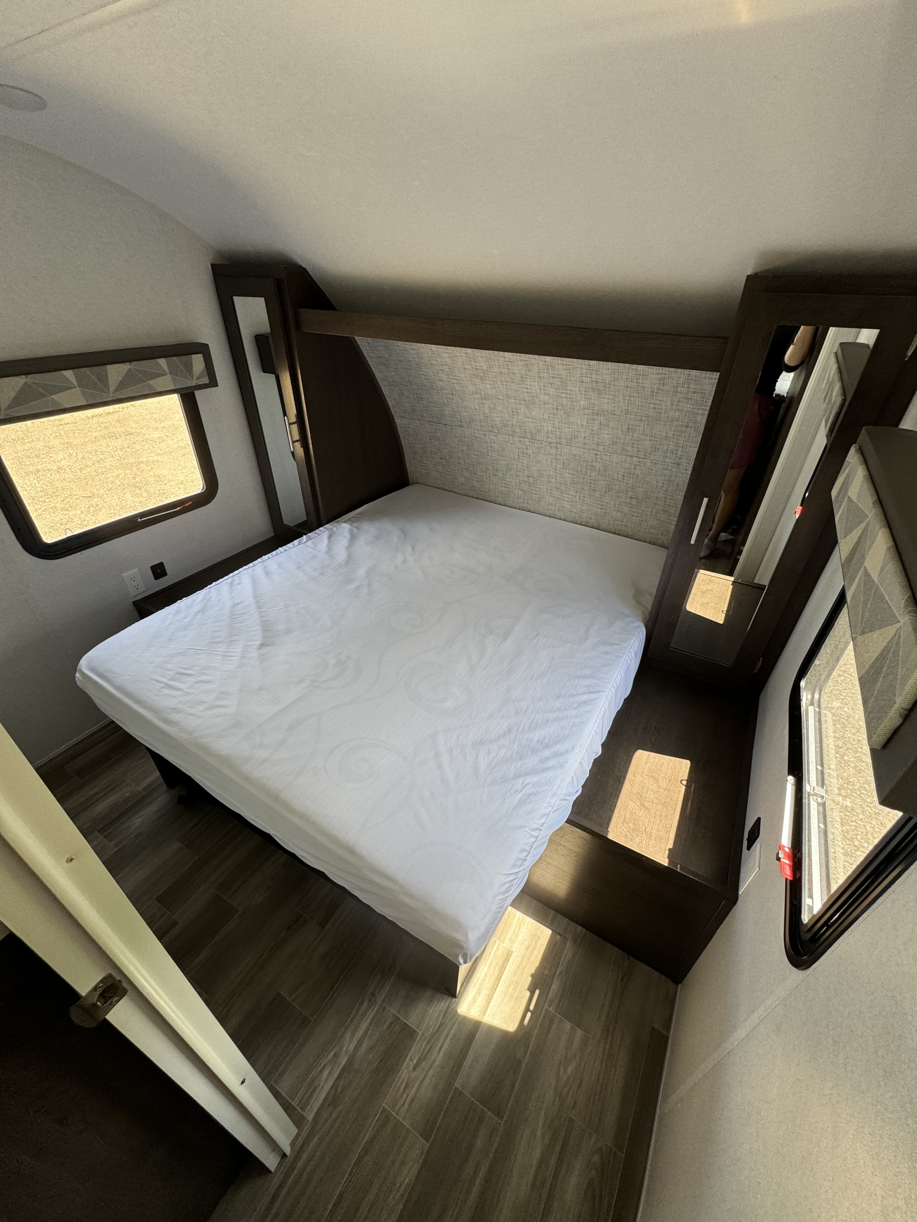 Bright RV rental bedroom features a white bed, mirrored closet, and windows, offering comfortable travel accommodation.. Forest River Salem Cruise Lite 2019