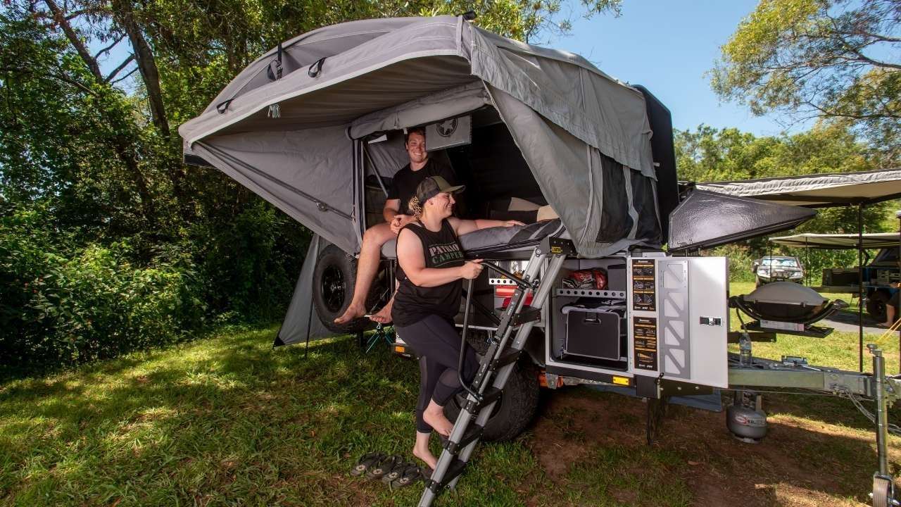 Couple enjoys a spacious rooftop tent on a camping trailer, perfect for an RV rental adventure. Outdoor glamping with storage and BBQ.. Patriot Campers Patriot Campers Trailer 2022