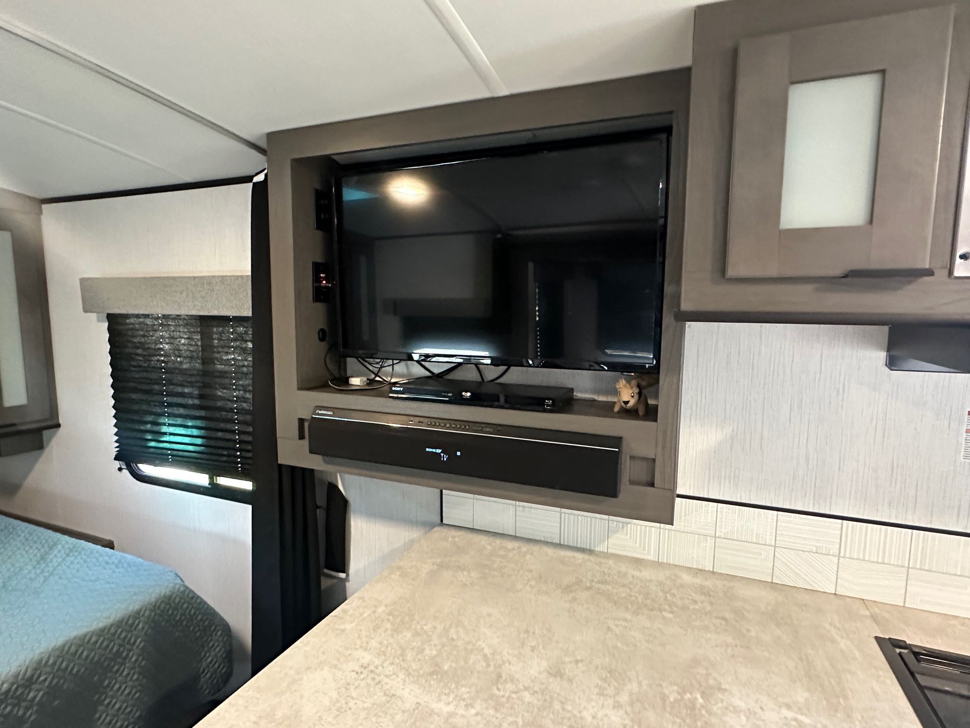 RV rental interior with a wall-mounted Furrion TV and soundbar above a bed. Features an entertainment setup.. Cruiser RV MPG Ultra Lite 2022