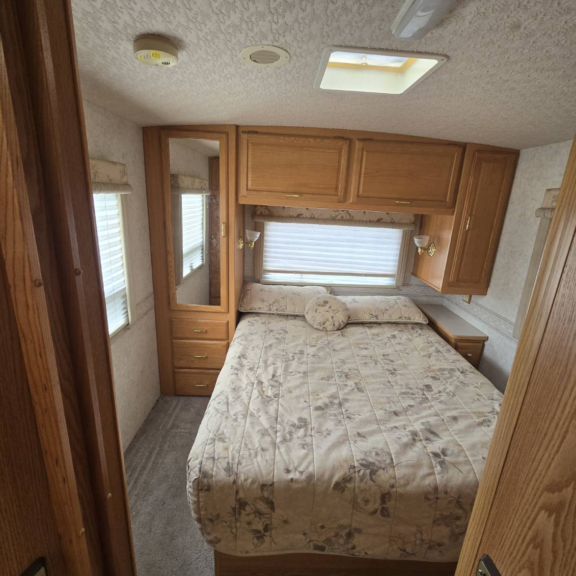 Comfortable RV rental bedroom showcasing a patterned bed, wood storage, windows, and a full-length mirror.. Winnebago Brave 2001