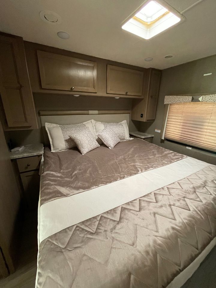 Step inside this cozy RV rental bedroom. It features a large bed, overhead storage cabinets, and a ceiling skylight.. Thor Windsport 2021