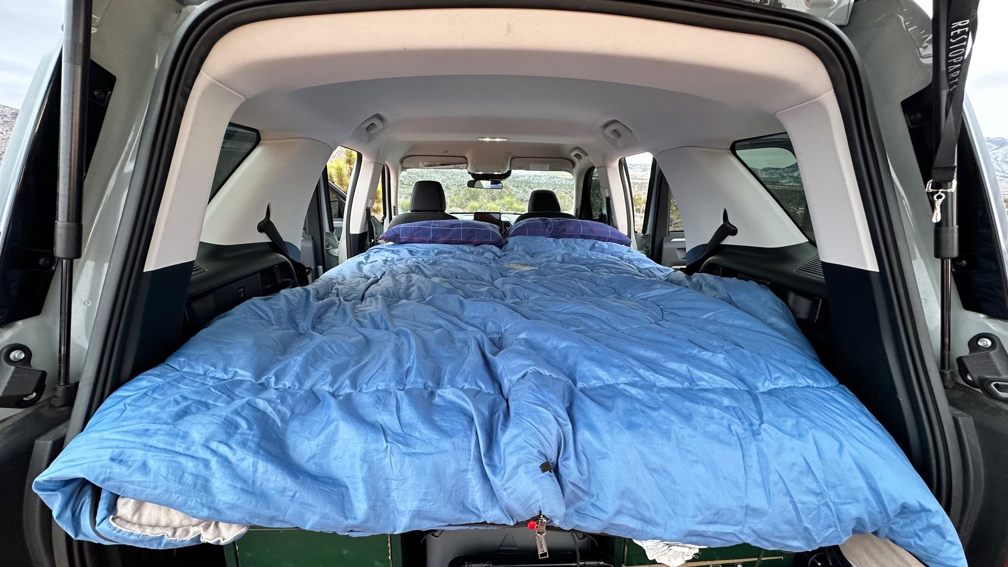 View inside SUV: cargo area converted into a bed with blue sleeping bag and pillows. Car camping comfort, like an RV rental experience.. Ford Bronco Sport 2022