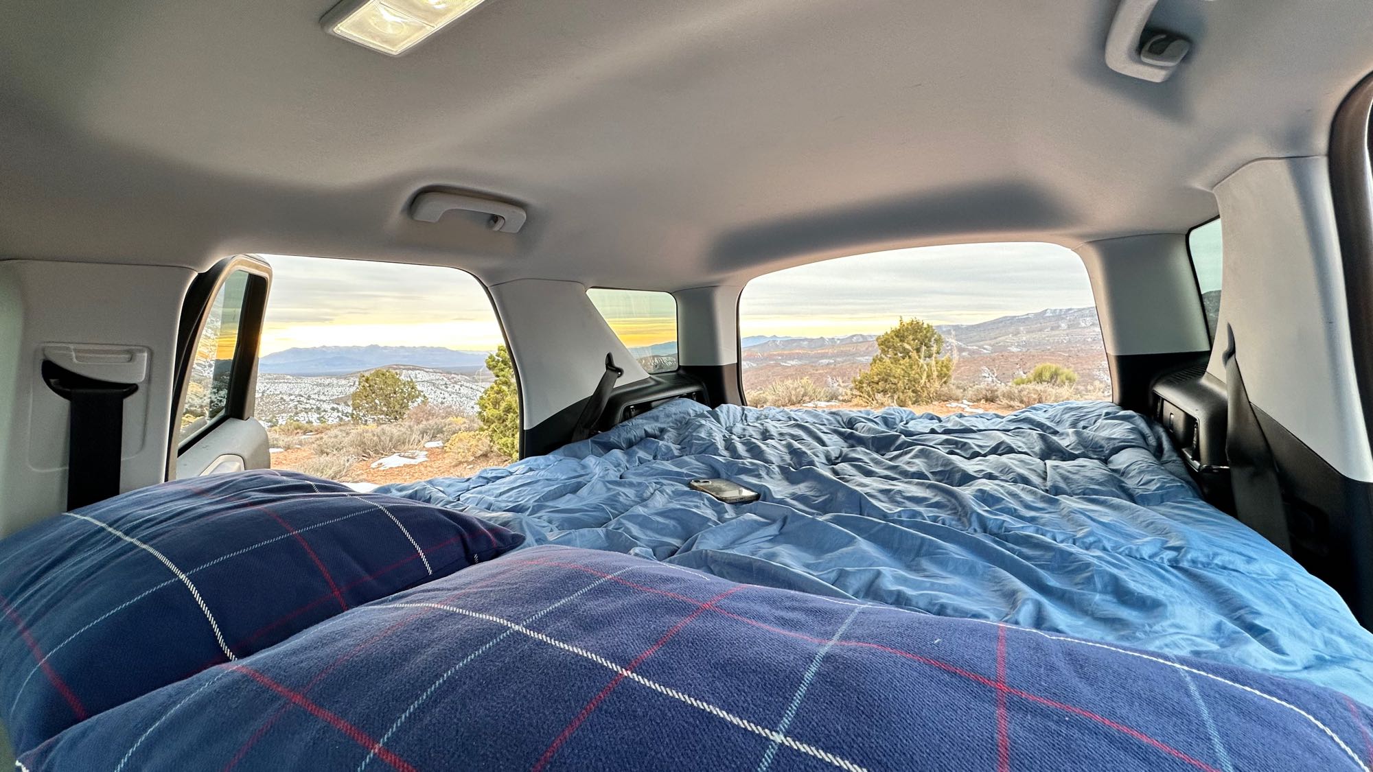 Interior of a parked vehicle with a cozy bed. Outside, a snowy desert and mountains at sunset. Consider an RV rental!. Ford Bronco Sport 2022