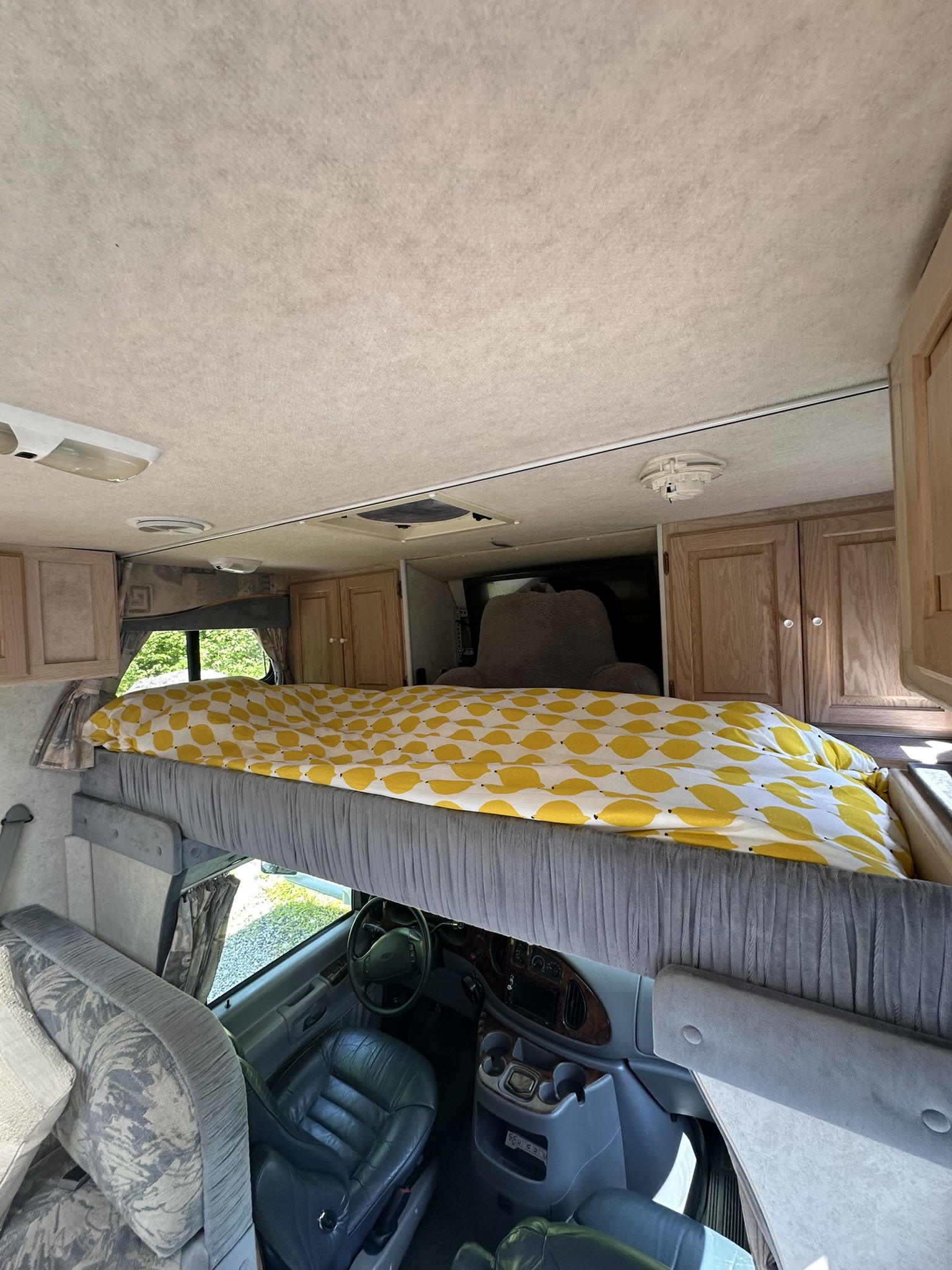 RV rental interior: Cab-over bunk with a vibrant yellow patterned blanket, above the driver's seat and dashboard.. Bigfoot RV Bigfoot RV Motorhome 2000