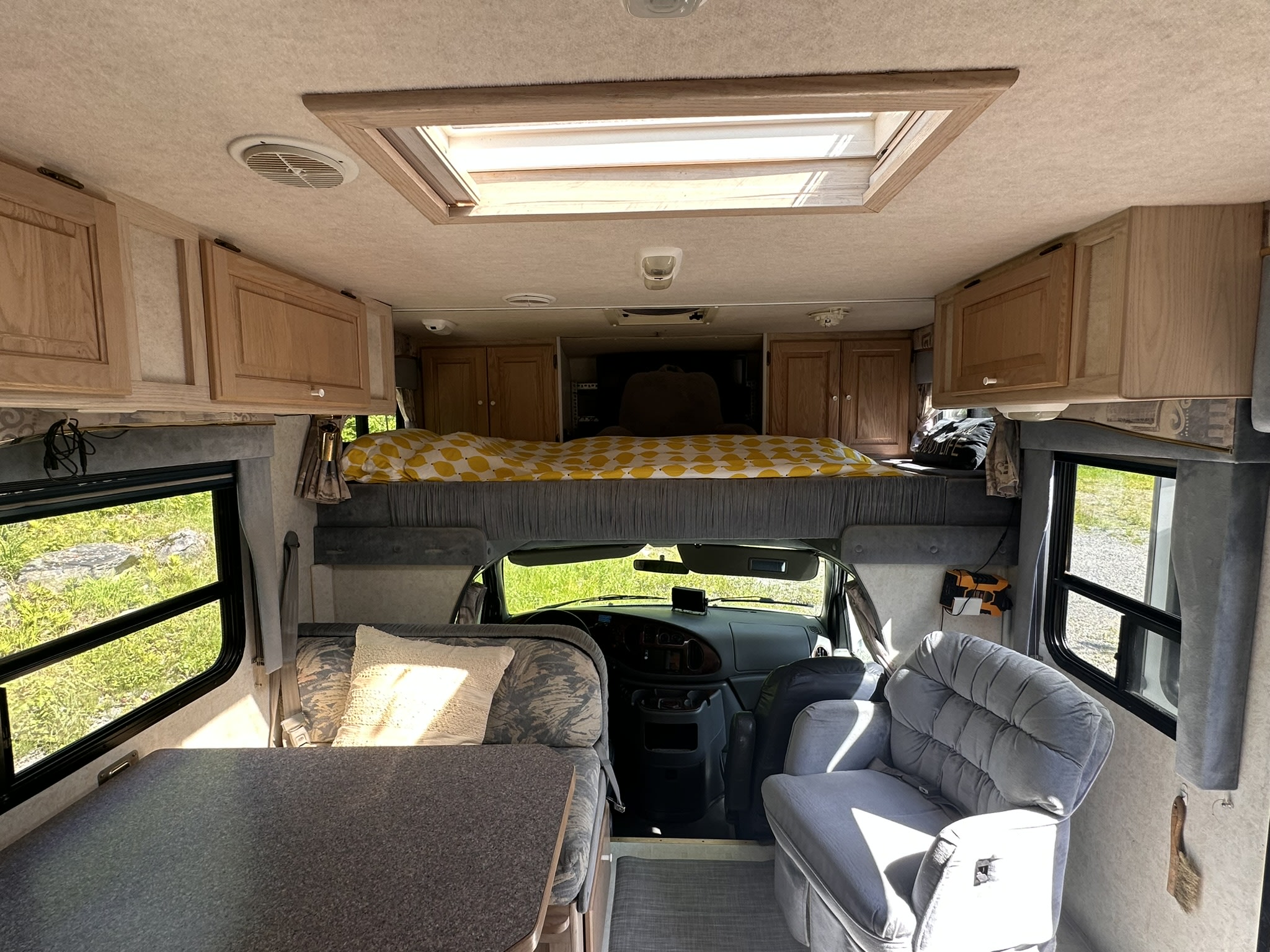 Bright RV rental interior: dining booth, bed, armchair, & windows showing nature.. Bigfoot RV Bigfoot RV Motorhome 2000