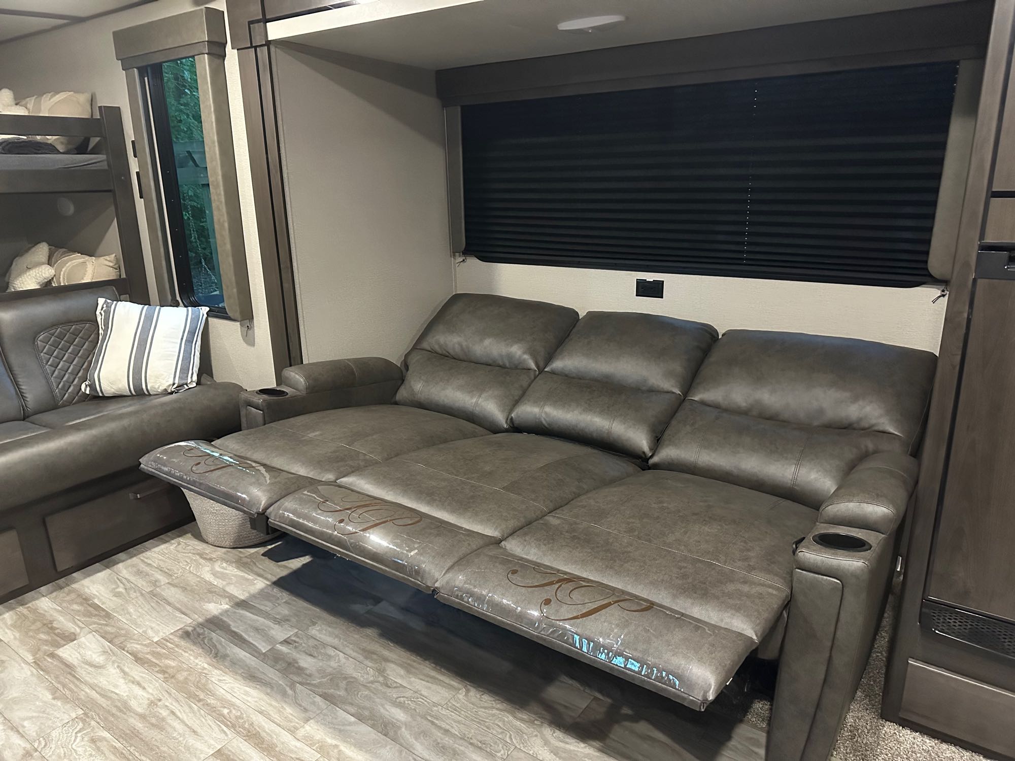 Comfortable RV rental living area featuring a grey reclining sofa with cup holders & protective covers, plus bunk beds.. Grand Design Transcend Xplor 2022