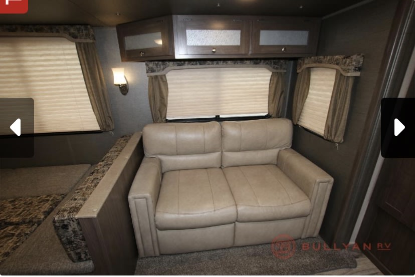 RV rental interior: cozy living space with light sofa, overhead cabinets, windows, and a partial dinette.. Keystone RV Hideout 2019