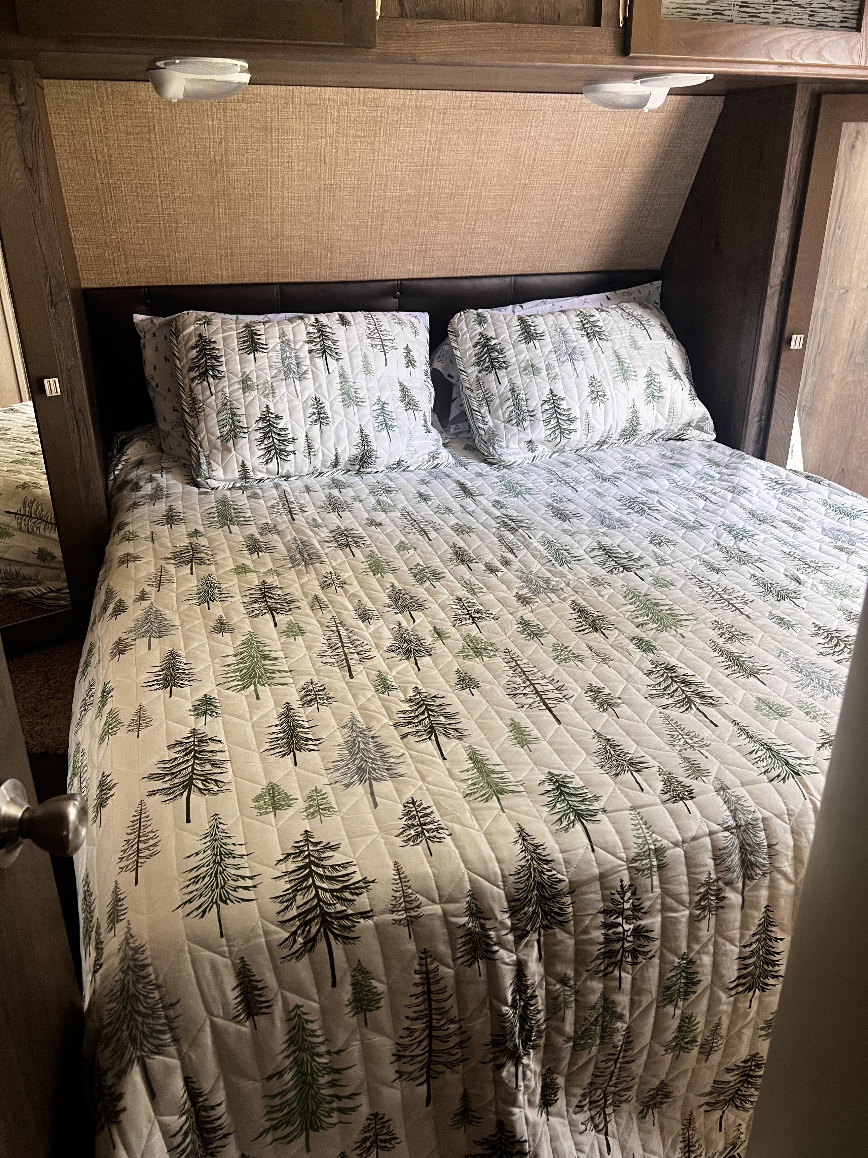 Cozy RV rental bedroom with pine tree bedding, headboard, overhead storage, and integrated lighting.. Dutchmen Kodiak 2015