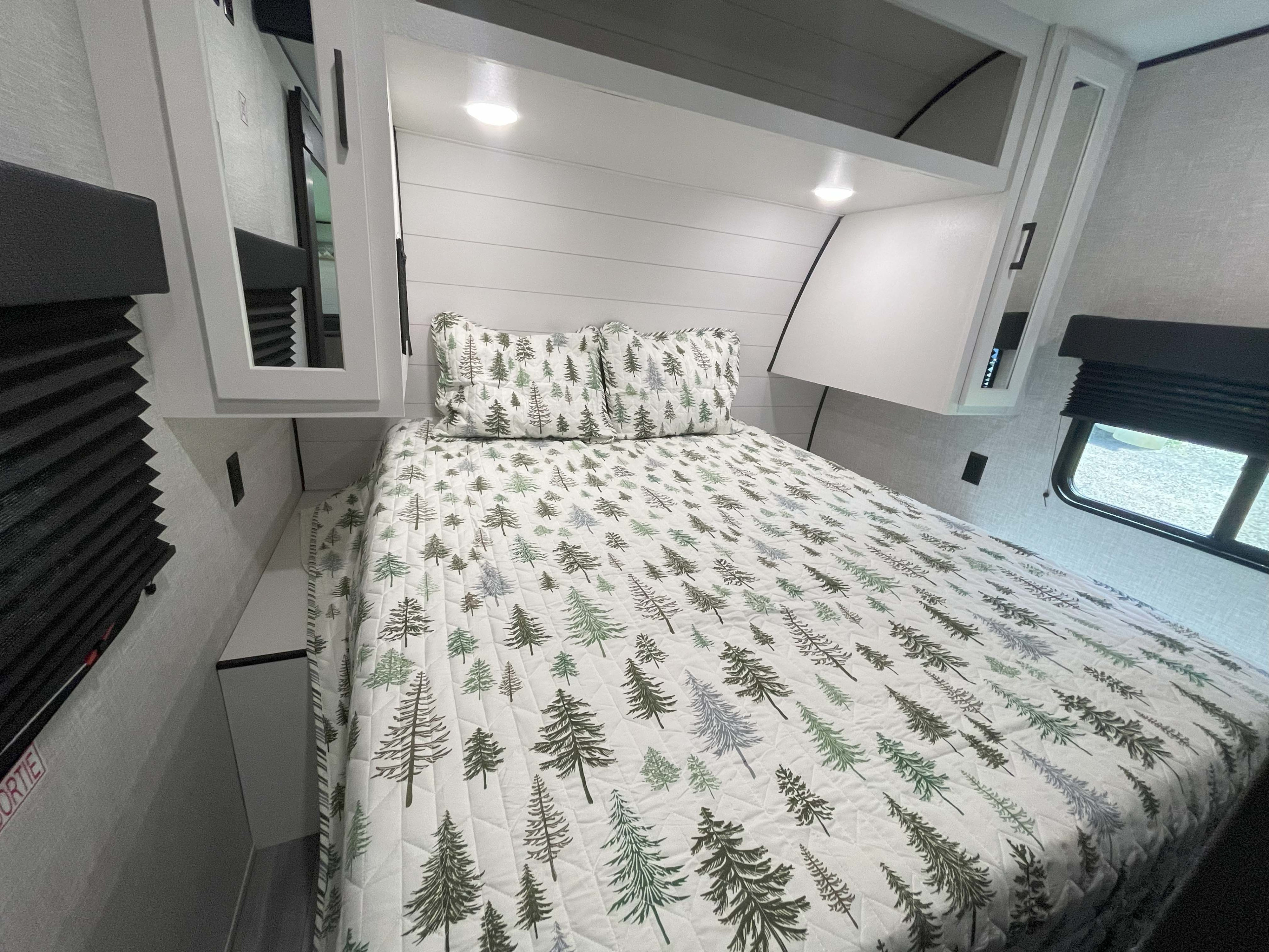 Cozy RV rental bedroom with a bed featuring nature-themed bedding, overhead cabinets, and window blinds.. Jayco Jay Flight SLX 2024