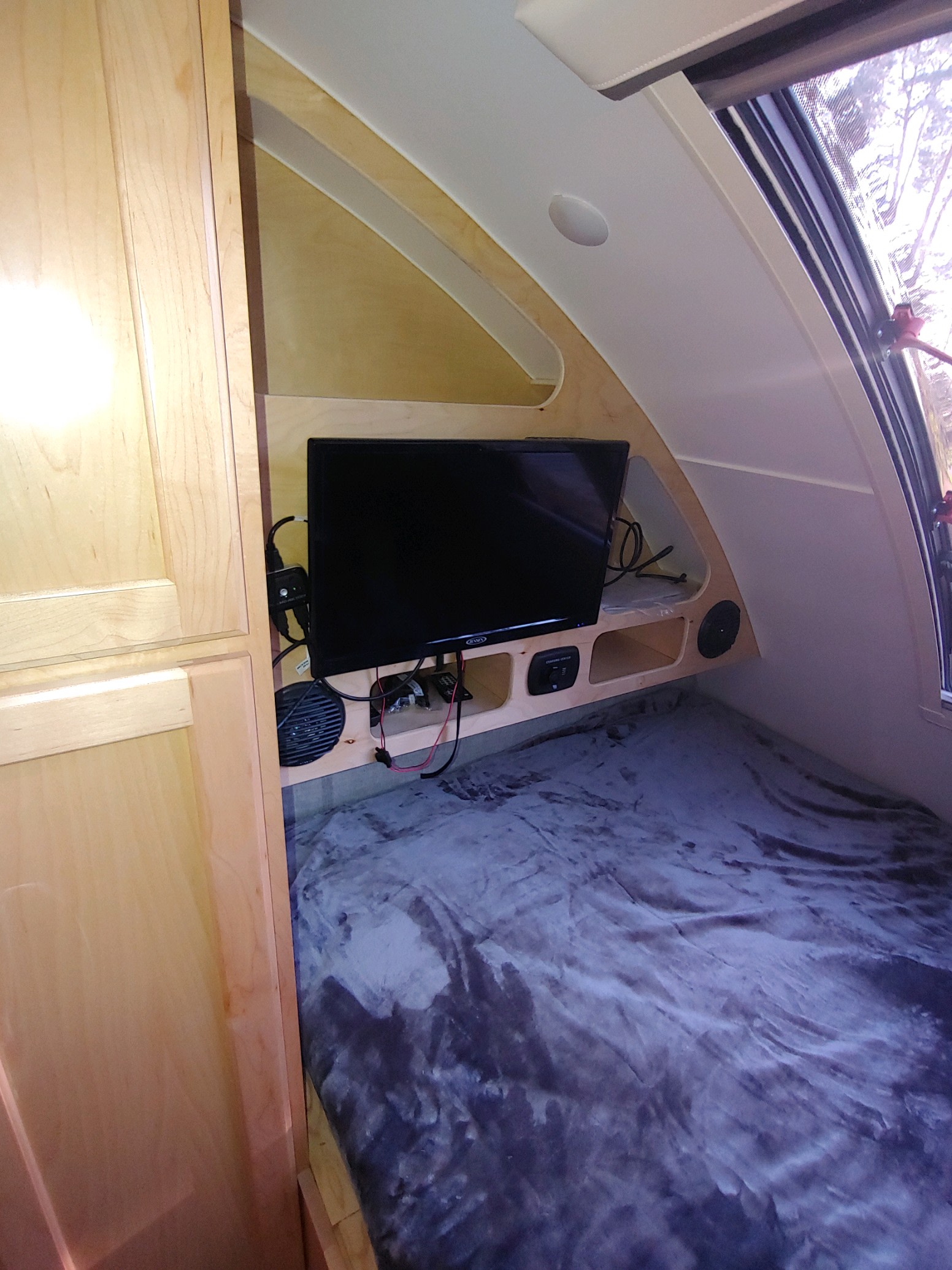 RV rental interior: cozy bed, wall-mounted TV & charging station in a light wood cabin. Ready for your adventure.. Little Guy Little Guy Trailer 2022