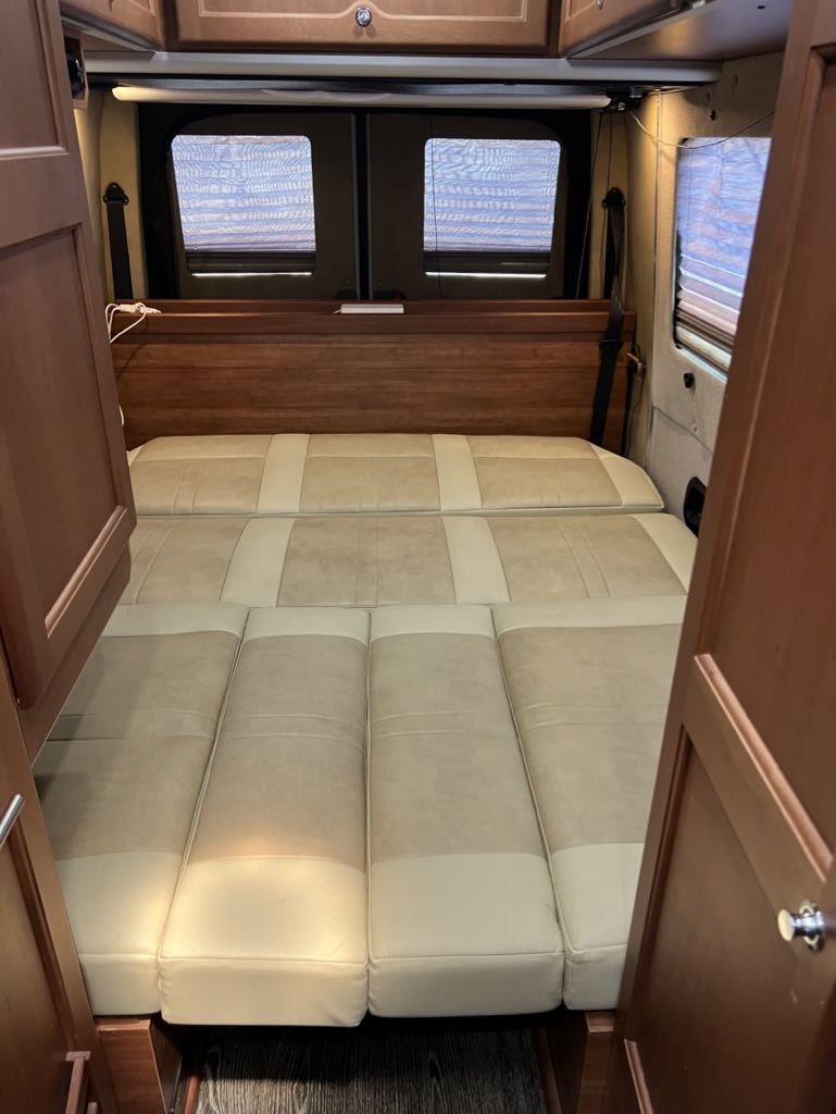 Spacious RV rental interior with a comfortable, multi-segment convertible bed, light cushions, and wood accents.. Roadtrek Roadtrek Class B 2017