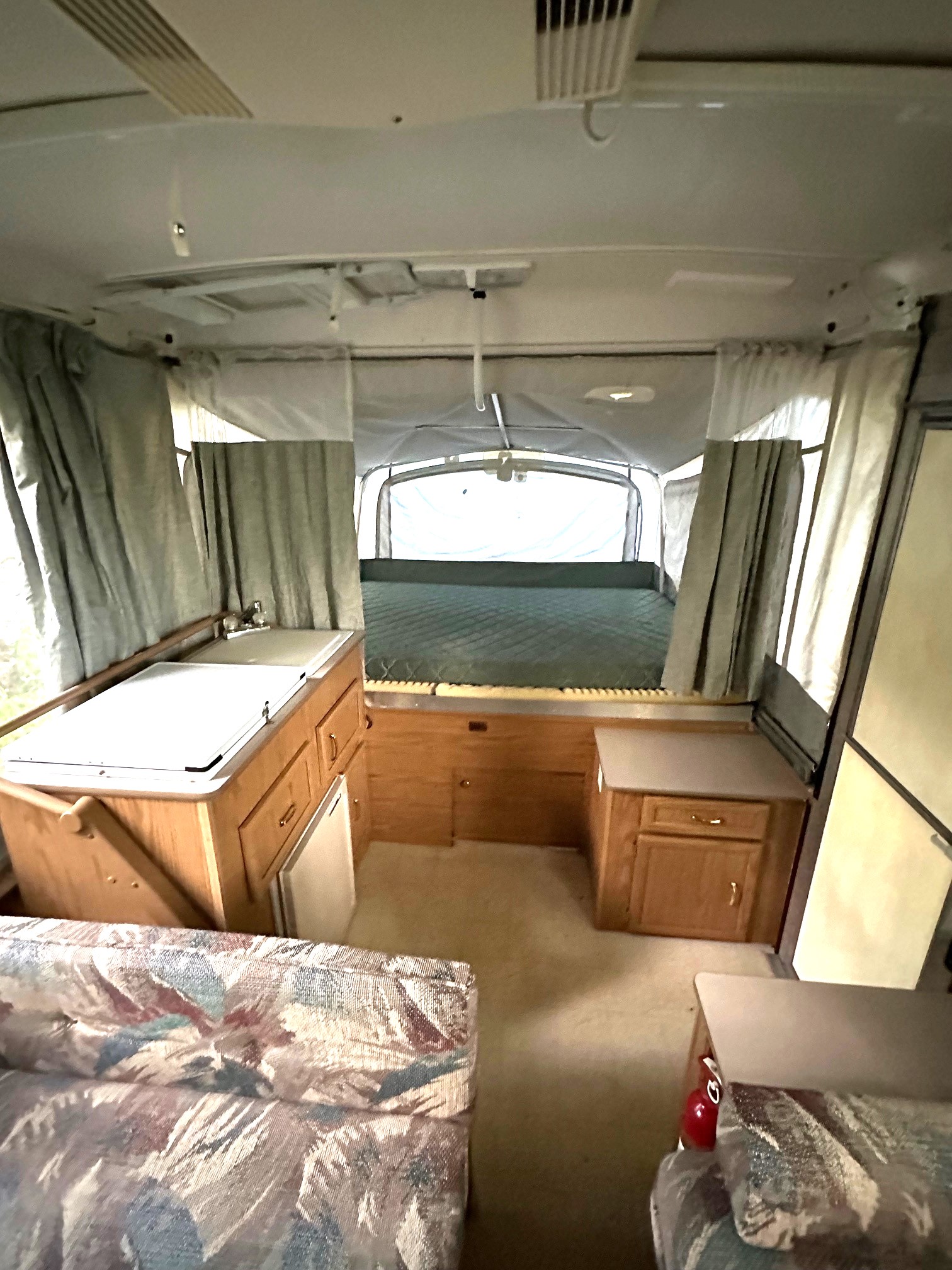 Inside a pop-up RV rental, featuring a kitchenette, rear bed, and patterned sofa for comfortable travel.. Fleetwood Coleman Cheyenne 2001