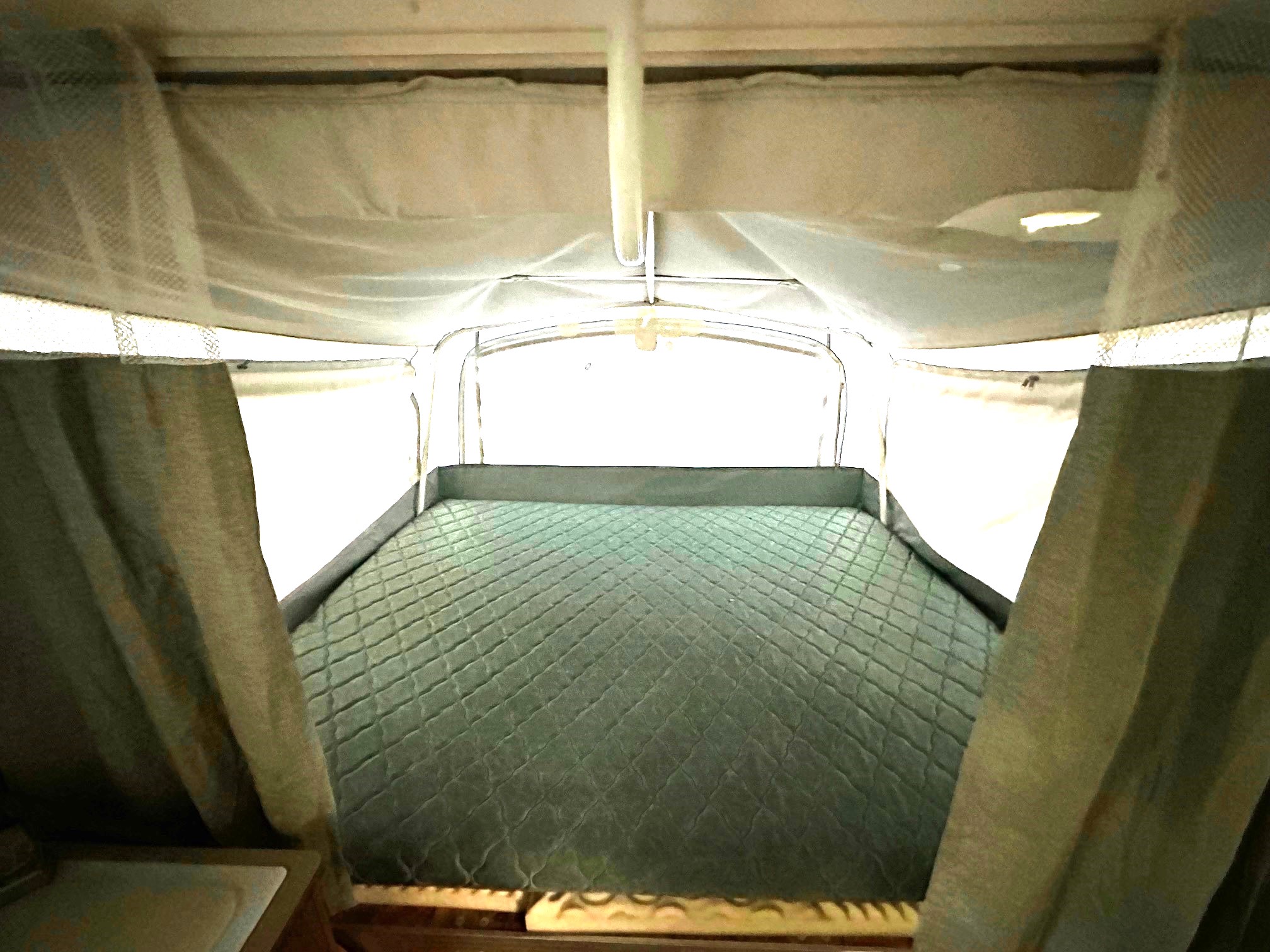 Cozy quilted bed inside an RV rental pop-up camper, ready for camping comfort.. Fleetwood Coleman Cheyenne 2001