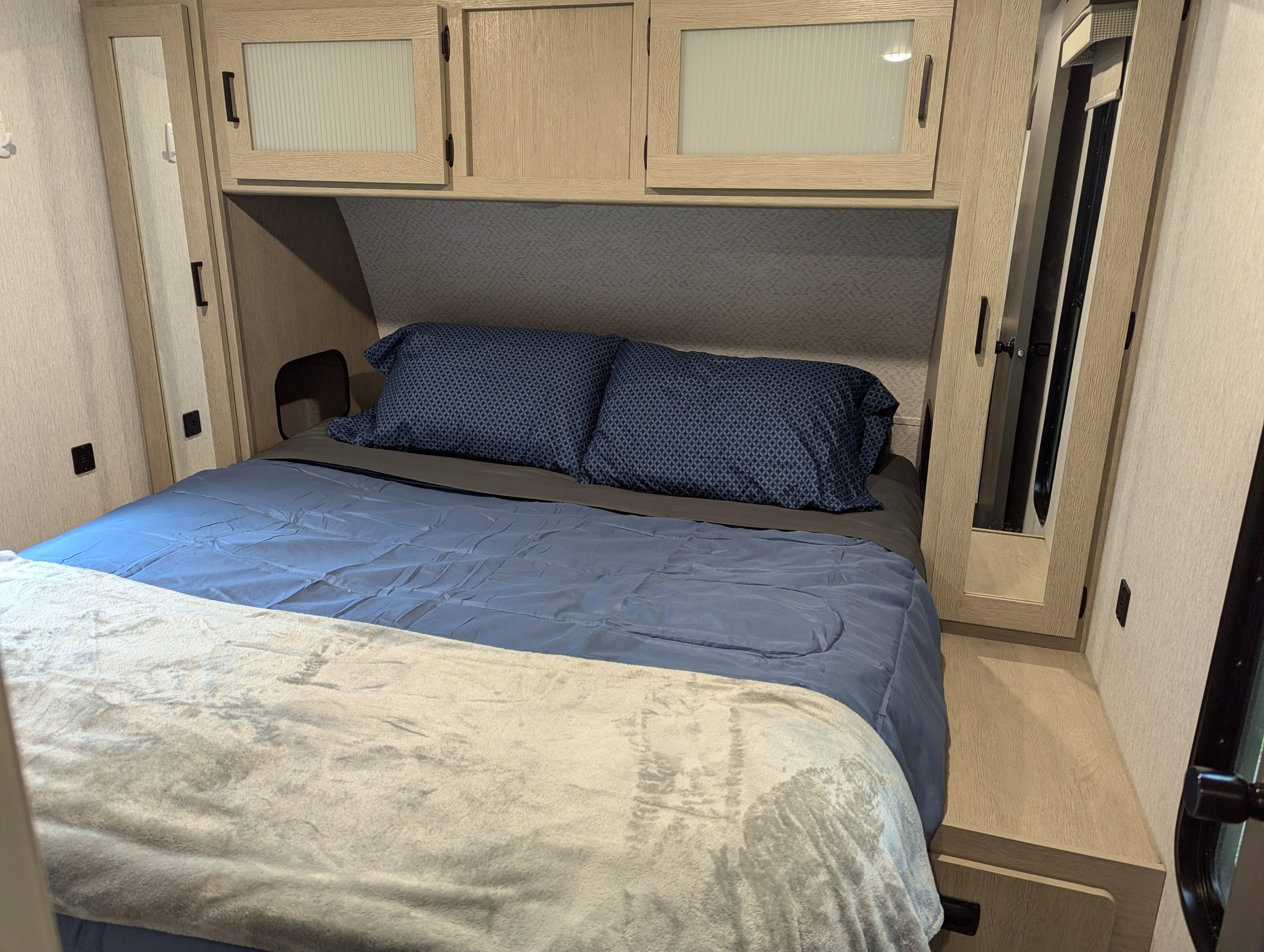 Experience comfort in this RV rental bedroom: blue comforter, patterned pillows, light wood cabinets, and a mirrored closet.. Forest River Wildwood 2023