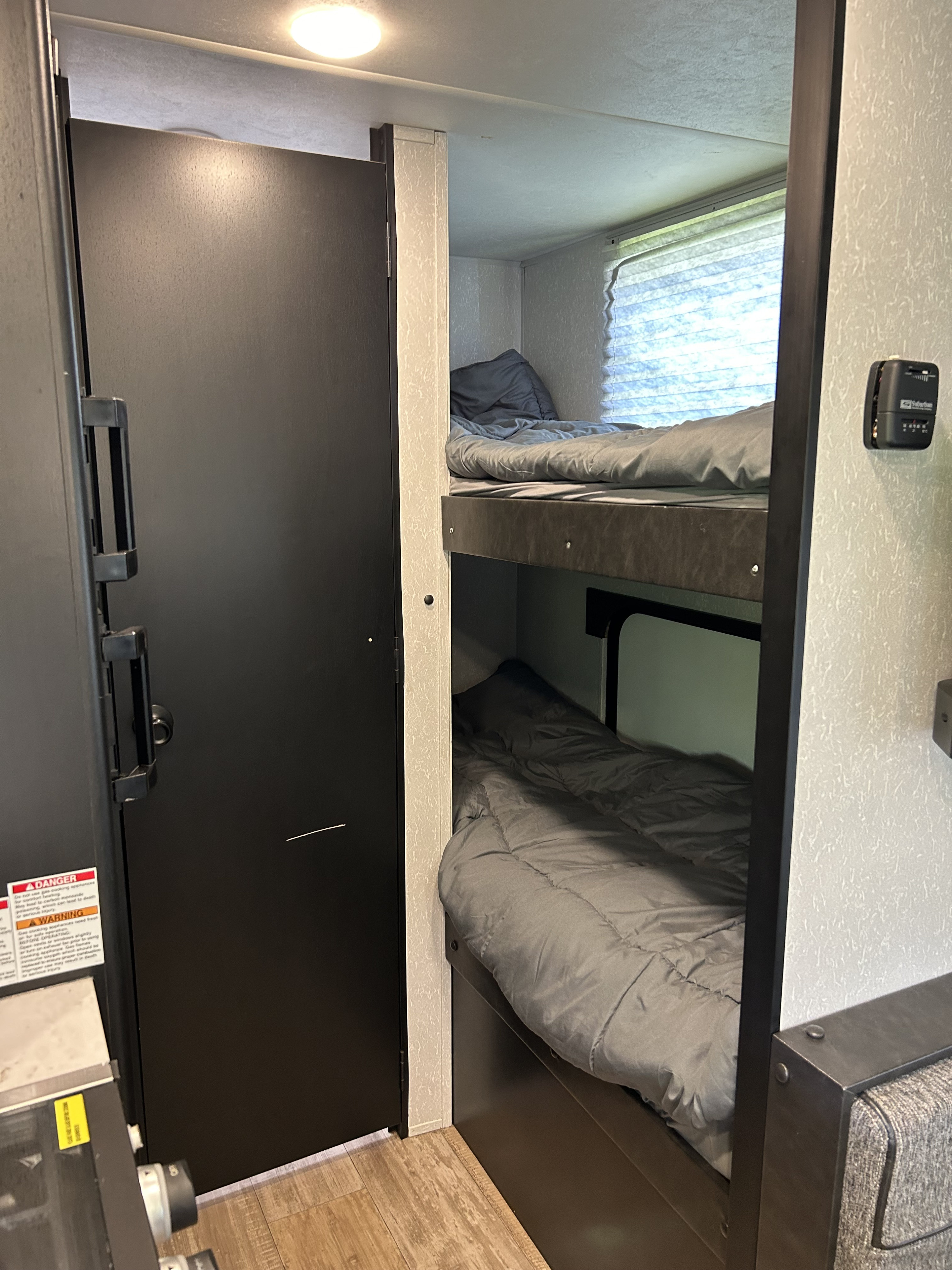 RV rental bunk bed sleeping area with dark door and window blinds. Grey bedding provides comfort for travelers.. Forest River Cherokee Wolf Pup 2022