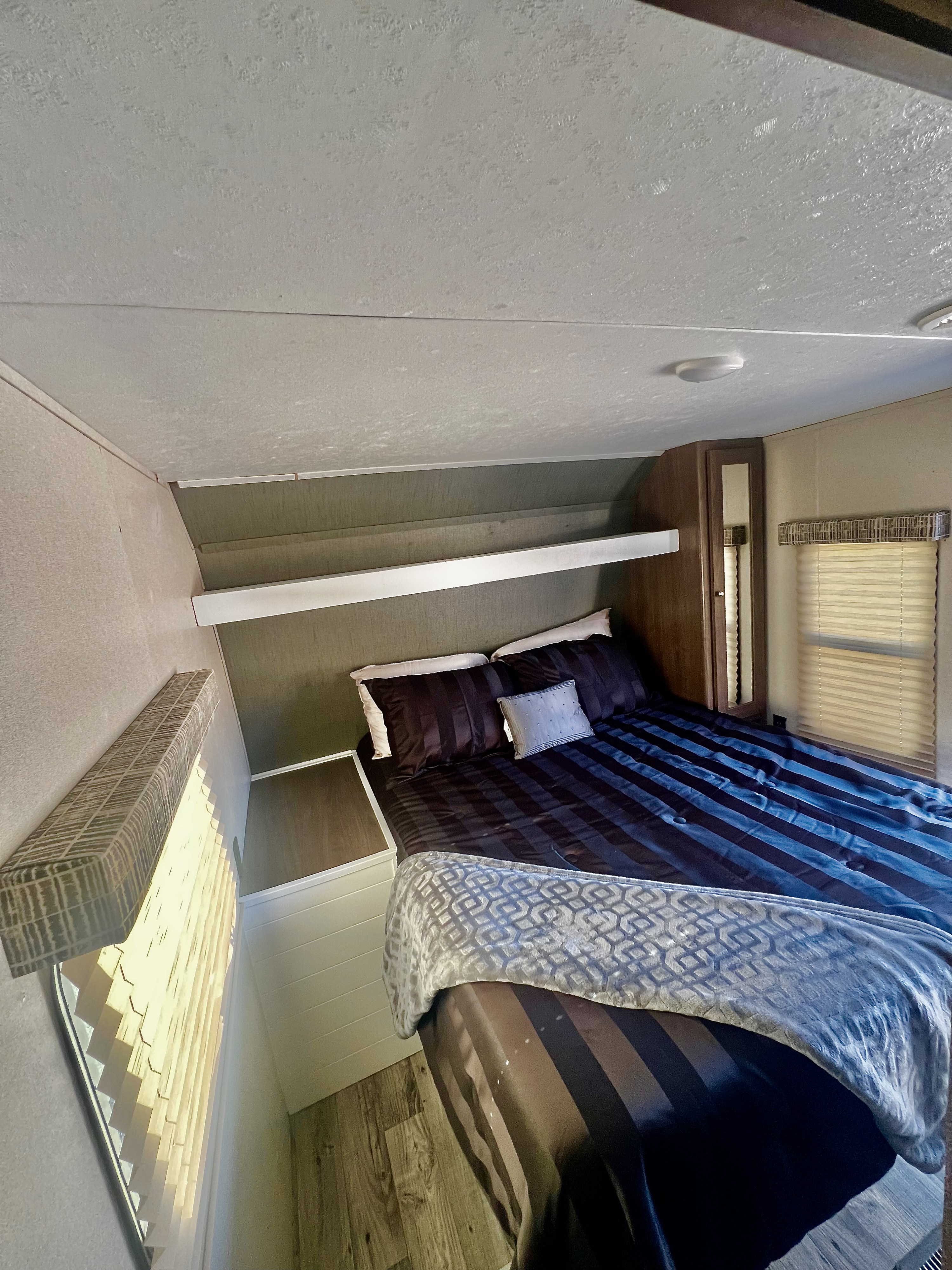 Cozy RV rental bedroom features a striped bed, storage shelf, and window blinds, ideal for your next trip.. Keystone RV Hideout 2018