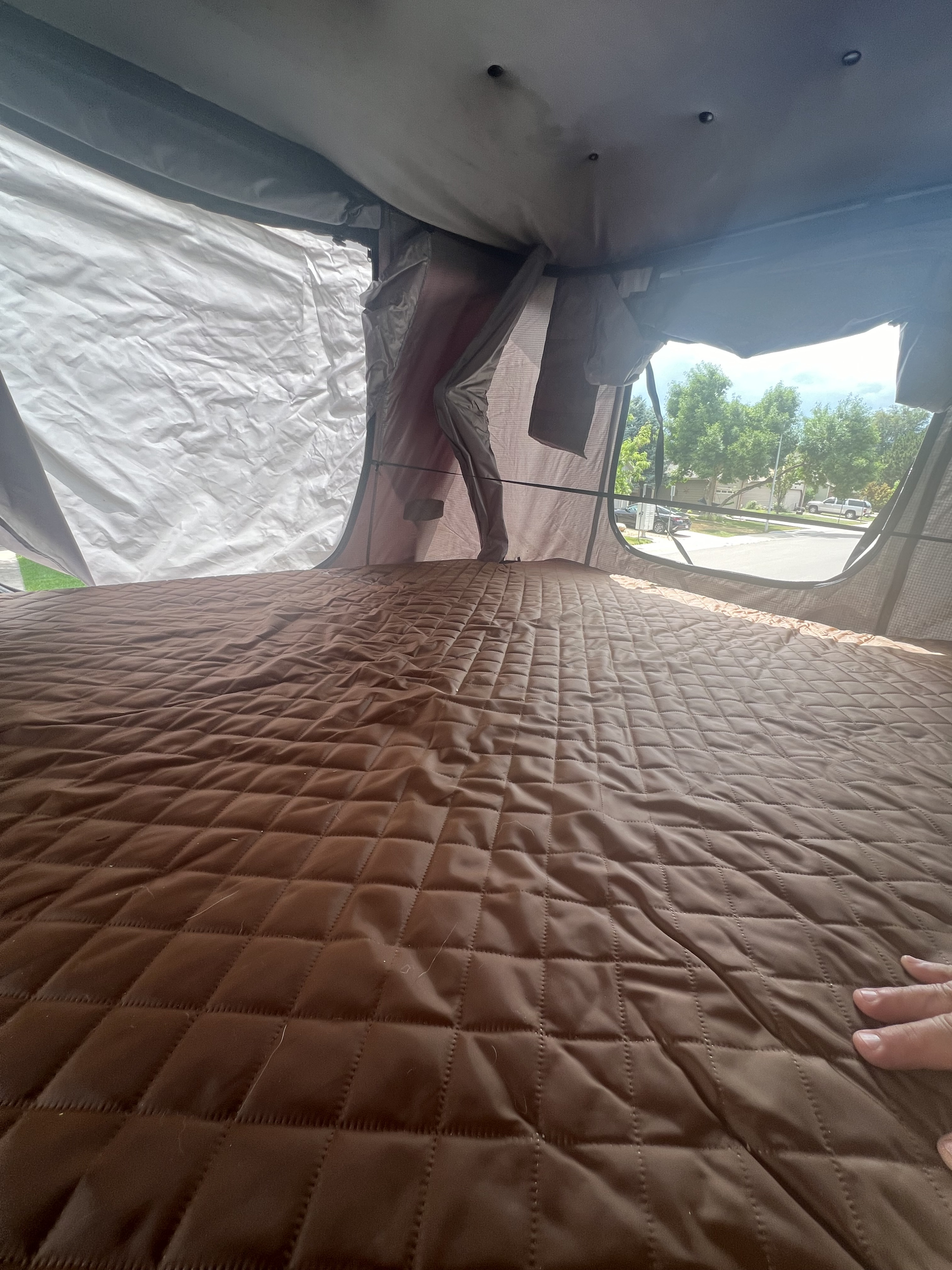 Cozy RV rental interior: a comfortable brown quilted mattress with a view of the outside. Ideal for camping.. Jeep Wrangler 2010