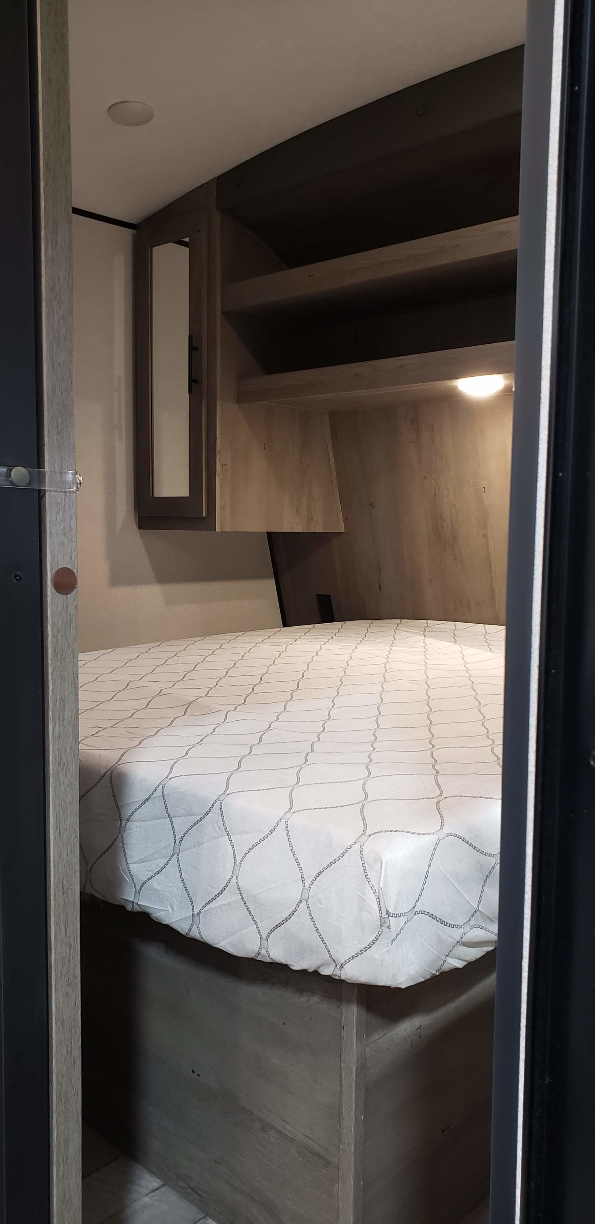 A compact yet well-appointed RV rental bedroom, offering a comfy bed, integrated shelving, and a mirrored cabinet.. Keystone RV Springdale 2021