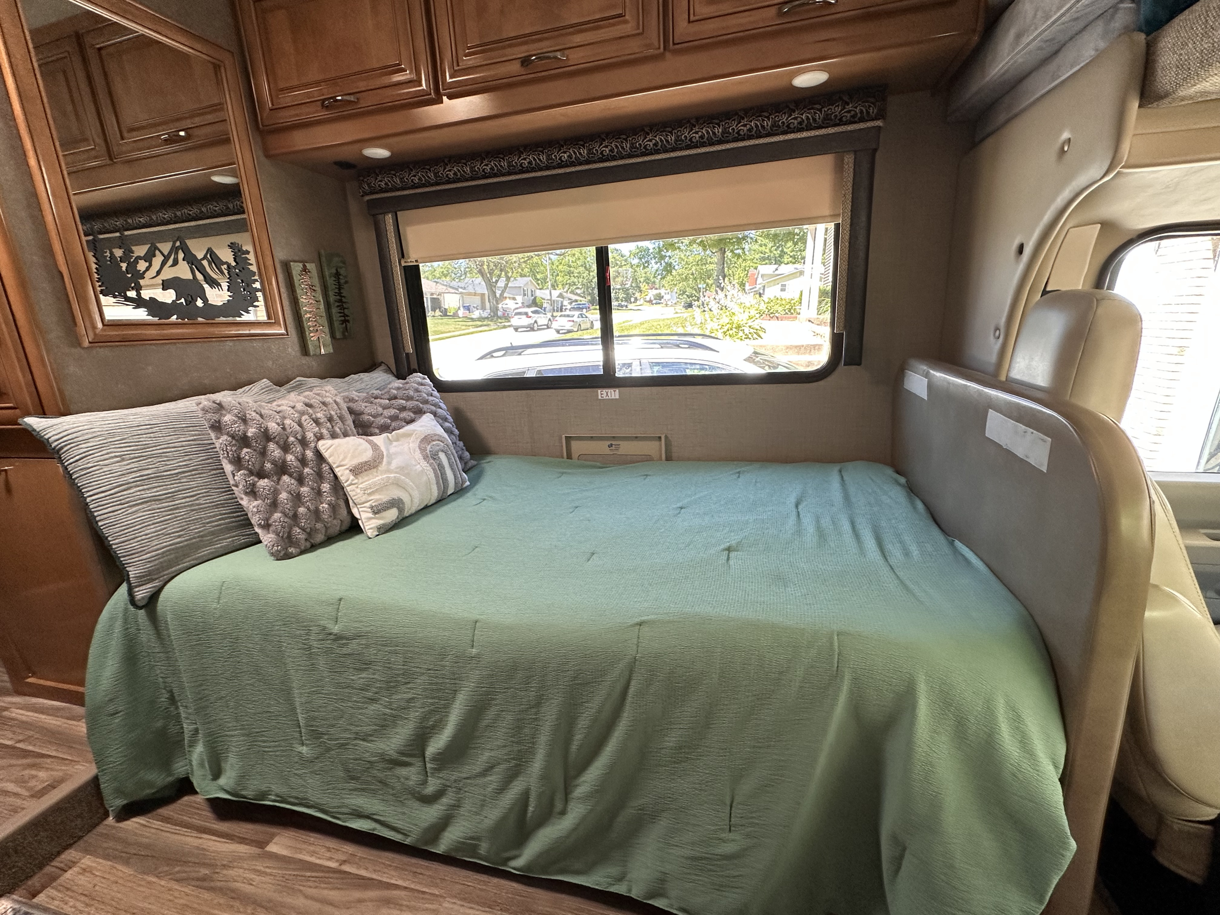 Step inside this RV rental's bedroom, showing a mint green bed, window with a neighborhood view, and wood cabinetry.. Thor Quantum 2018