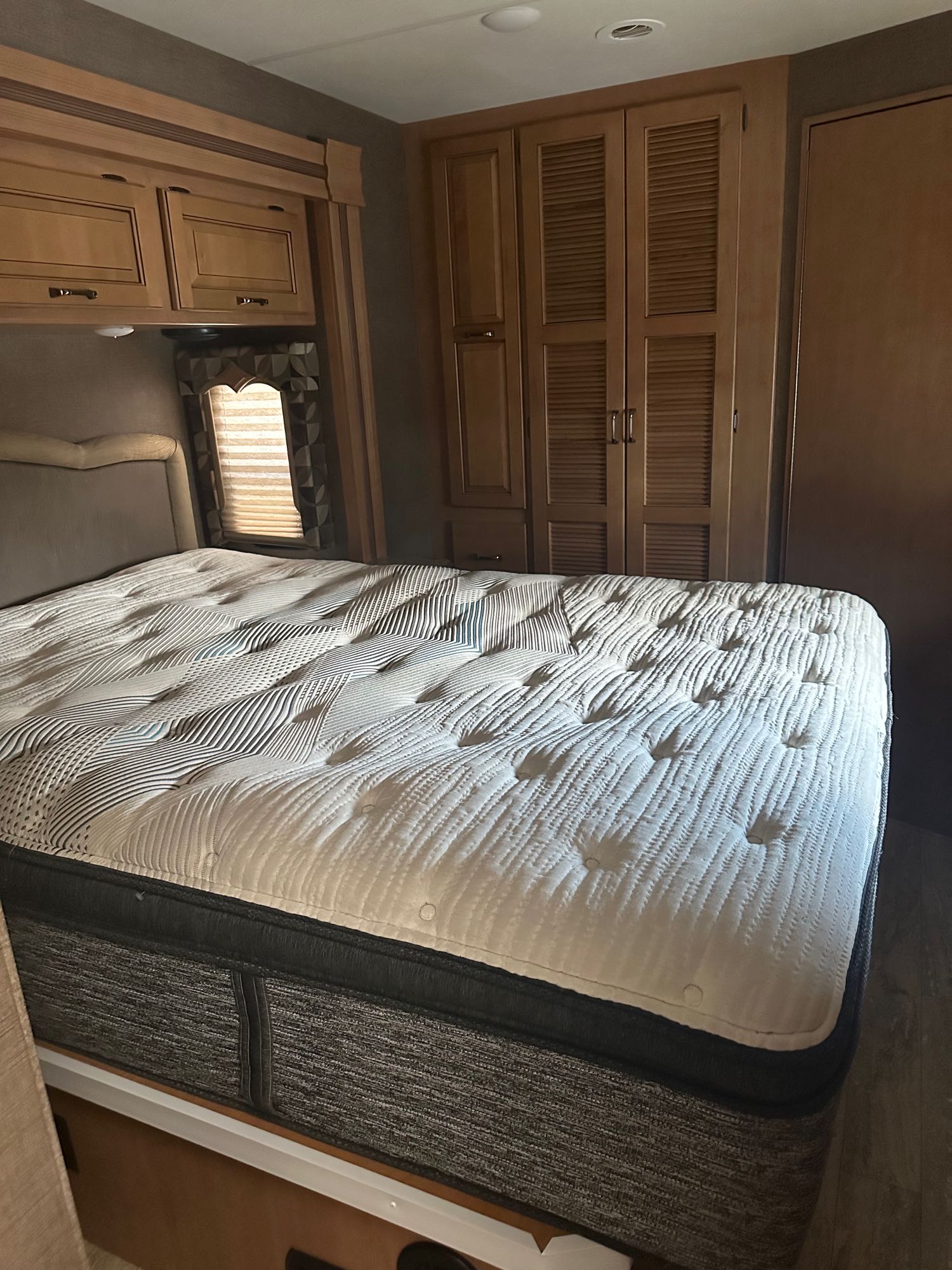 Comfortable RV rental bedroom with a large, plush patterned mattress, ample overhead storage, and a window for natural light.. Thor Hurricane 2017